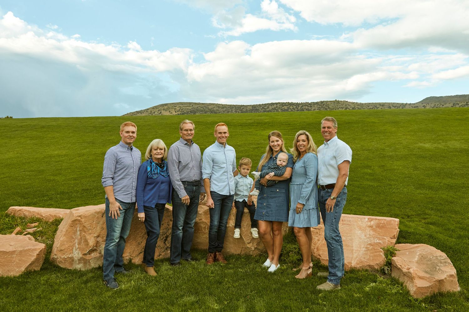 Group photo of people standing on large rocks with green hills and blue sky in background.