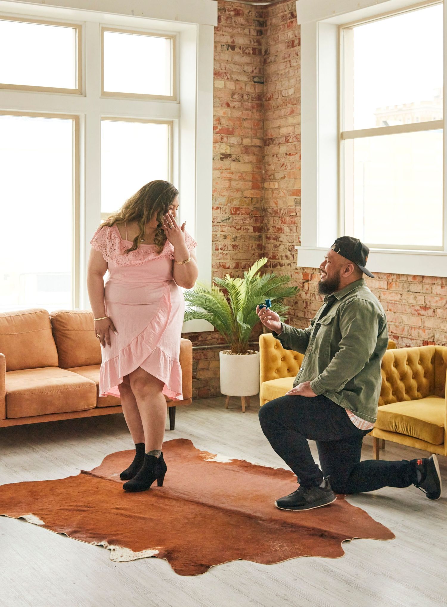 A proposal scene on a cowhide rug in an industrial-style loft with exposed brick walls.