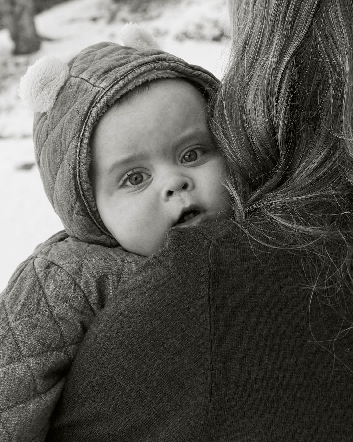Close-up black and white portrait of a baby in winter clothing looking over shoulder.