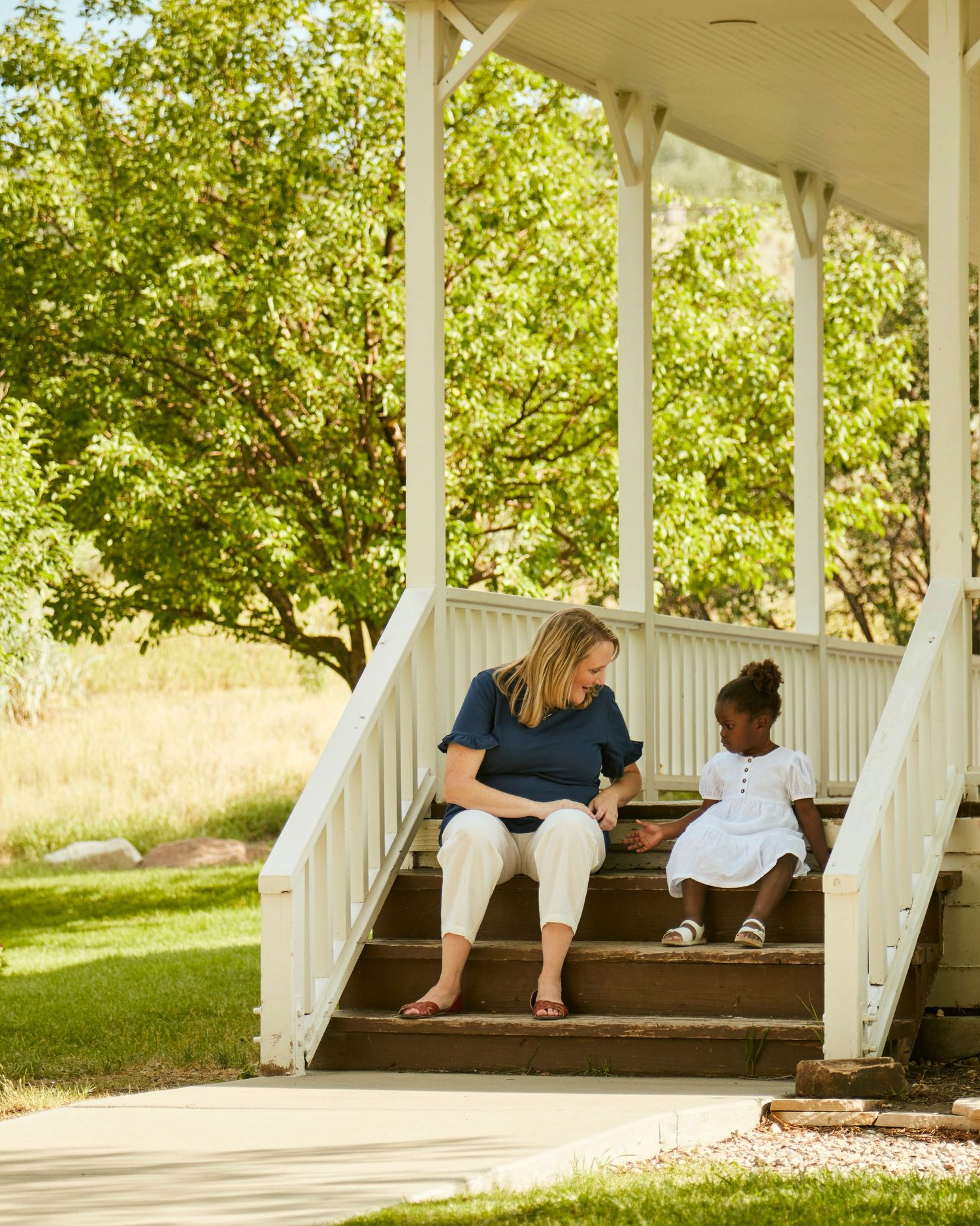 Two people sitting on white porch steps having a conversation on a sunny summer day.