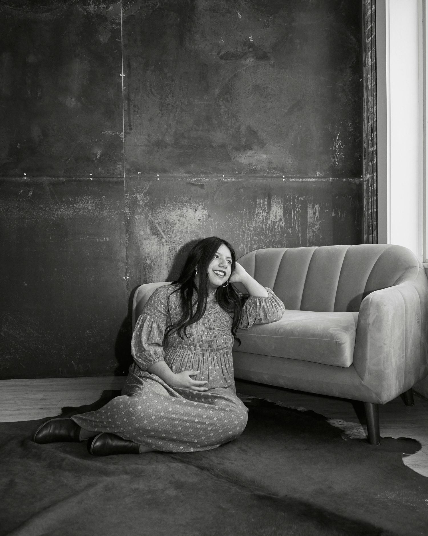 Person in polka dot dress sitting by vintage couch in moody black and white photo.