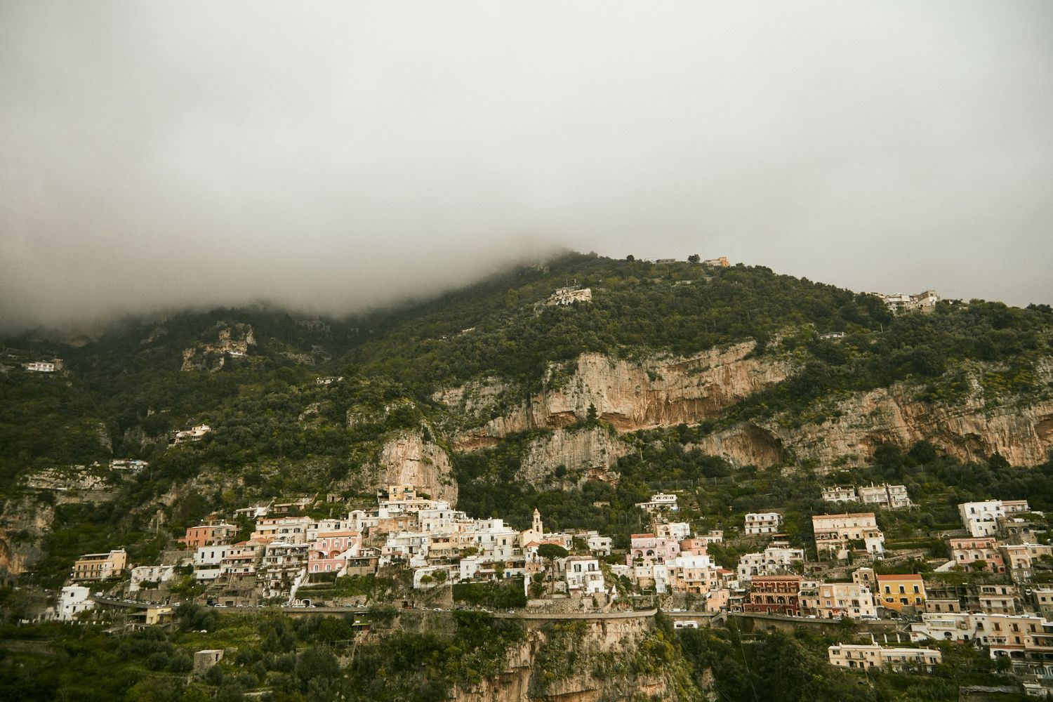Cliffside Mediterranean village with white buildings nestled in foggy mountain landscape.