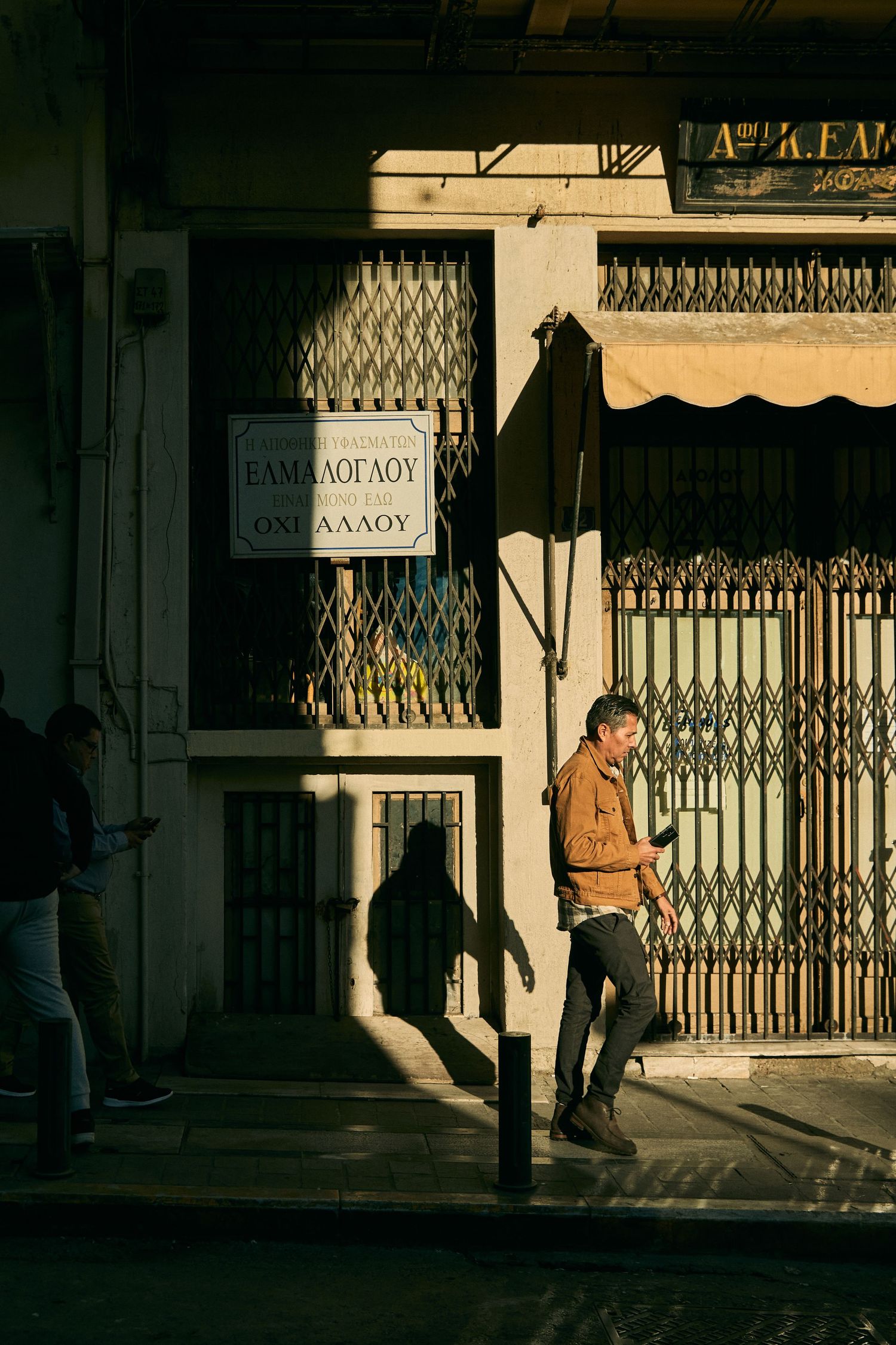 Sunlight casting dramatic shadows on a street corner with metal security gates.