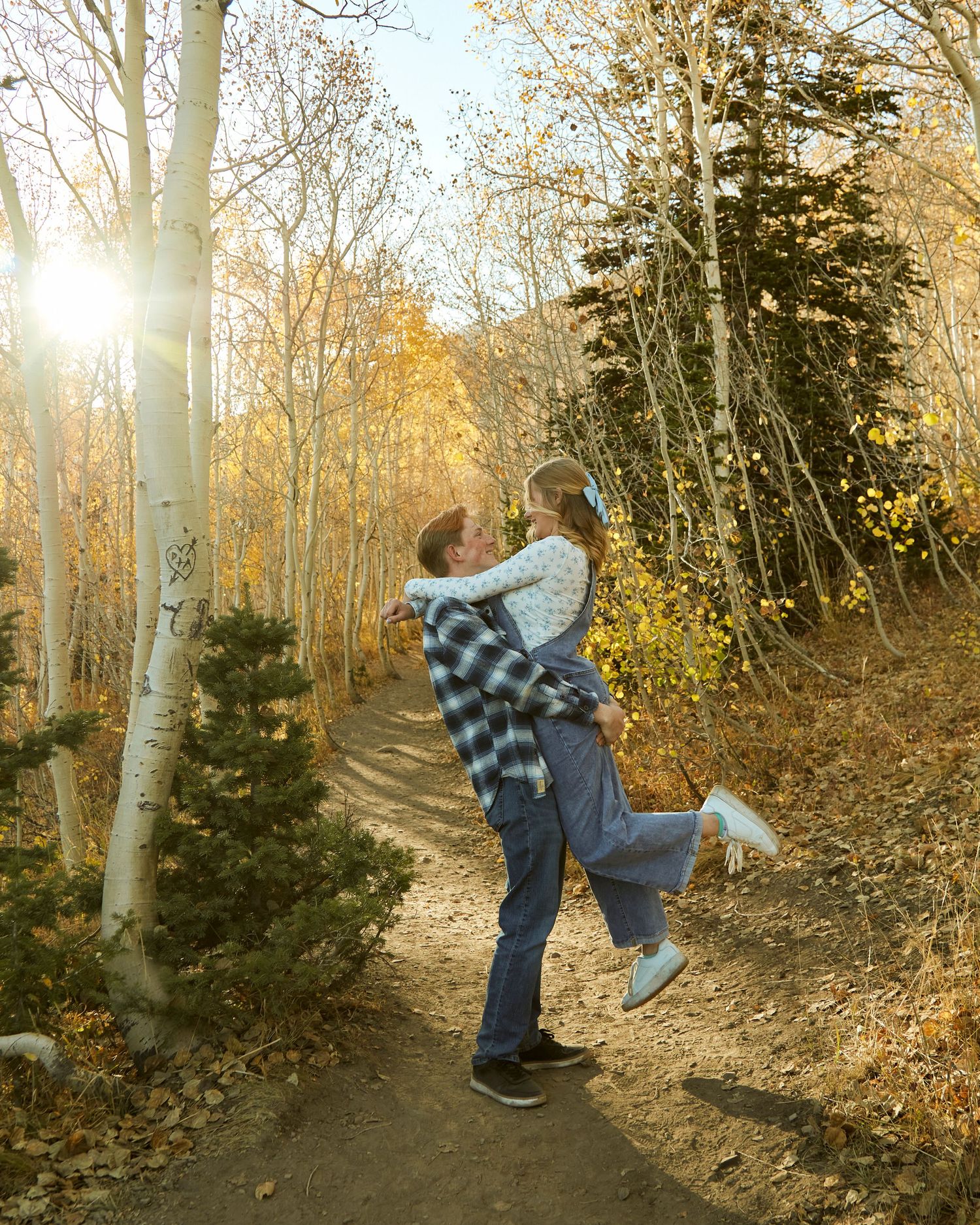 Couple embracing on an autumn trail with sunlight filtering through aspen trees.