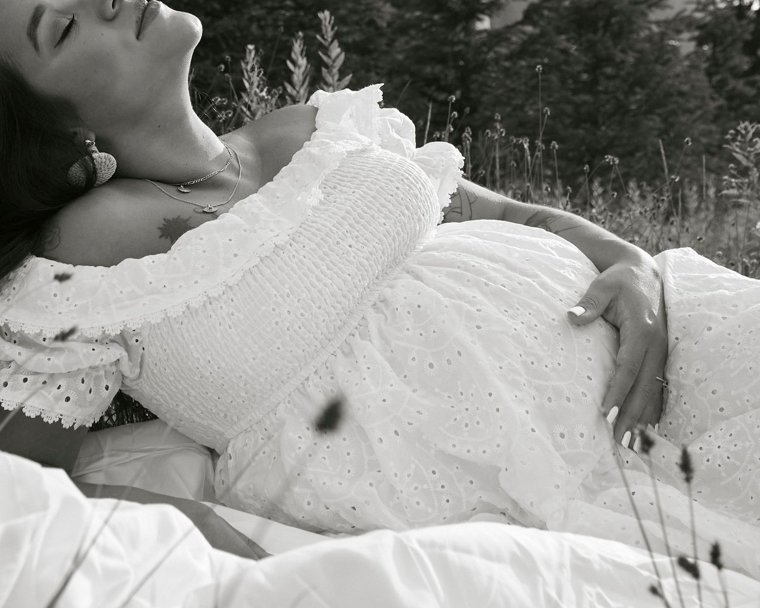 Dreamy black and white portrait of woman in lace dress reclining outdoors.