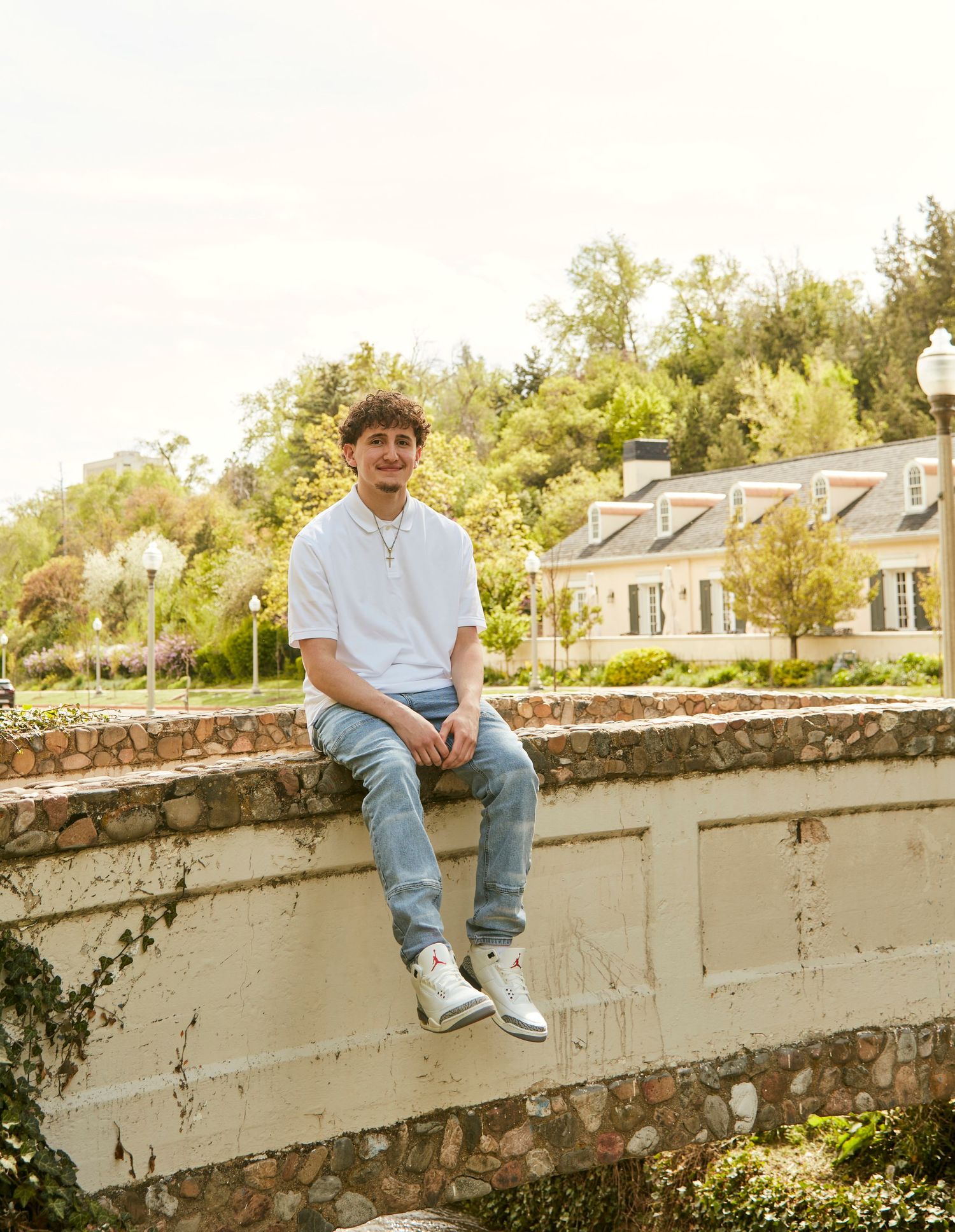 Person in casual attire sitting on stone wall with historic buildings in background.