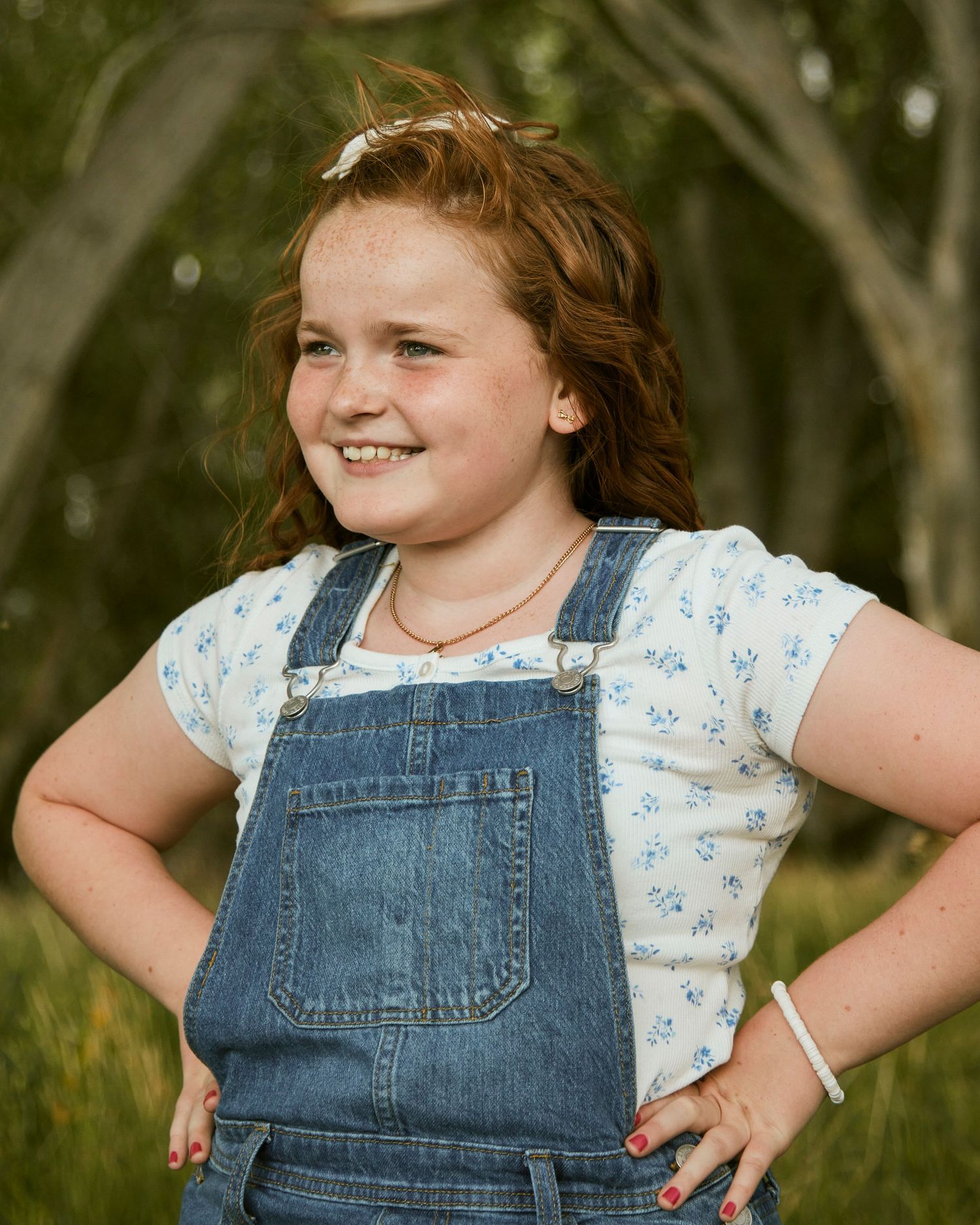 A candid portrait with floral top and denim overalls against a nature backdrop.