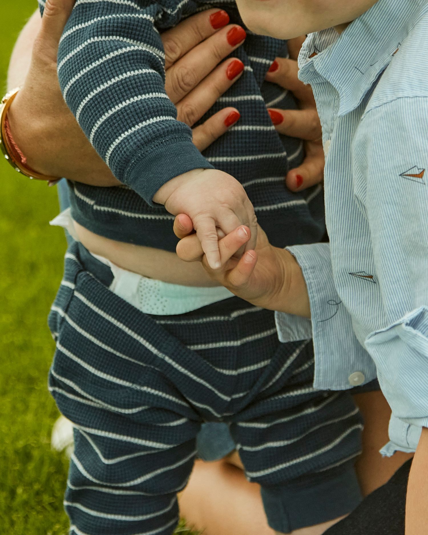 Close-up of hands holding small child in striped outfit outdoors.
