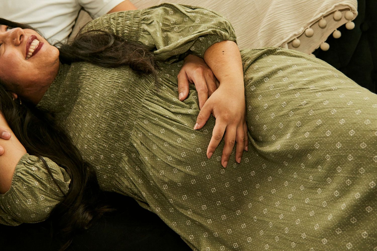 Woman in green polka dot dress reclining on couch while touching her pregnant belly.