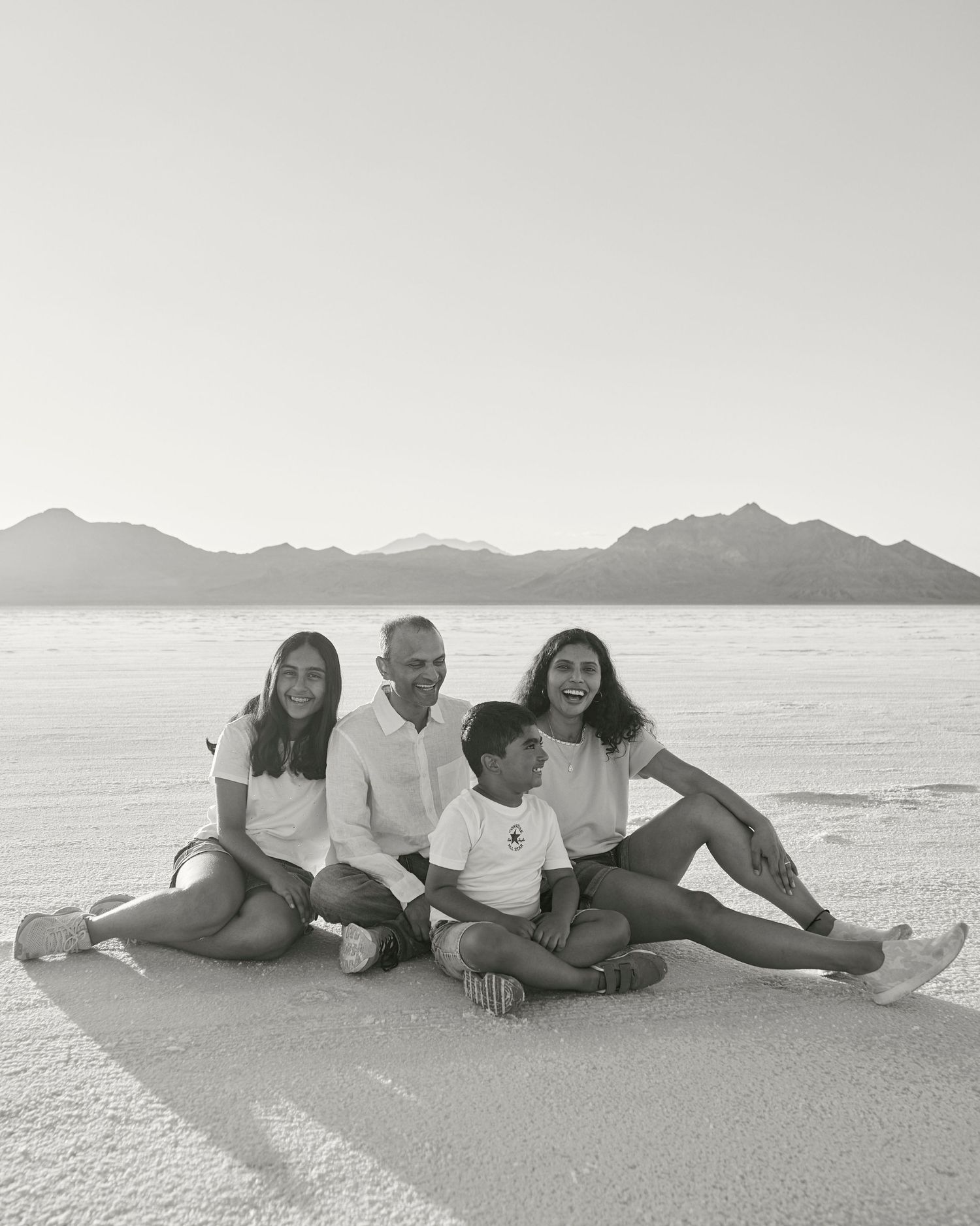 Family sitting together on white salt flats with mountain range in background.