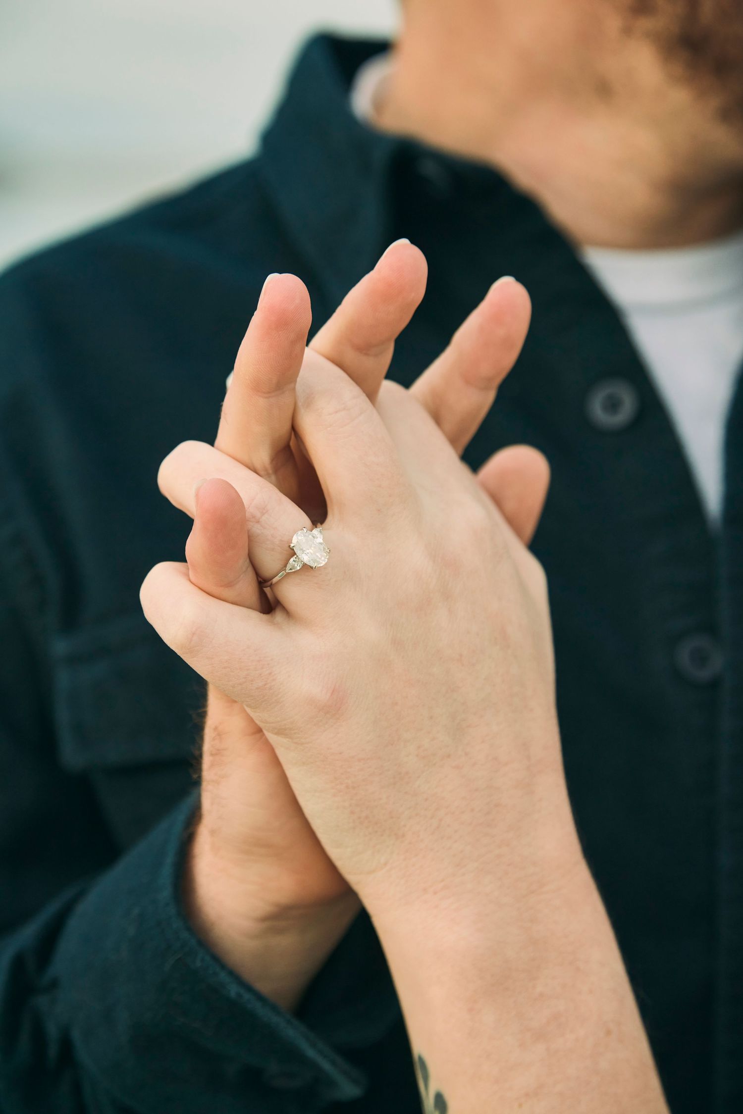 Close-up of hands with engagement ring intertwined against a dark jacket.