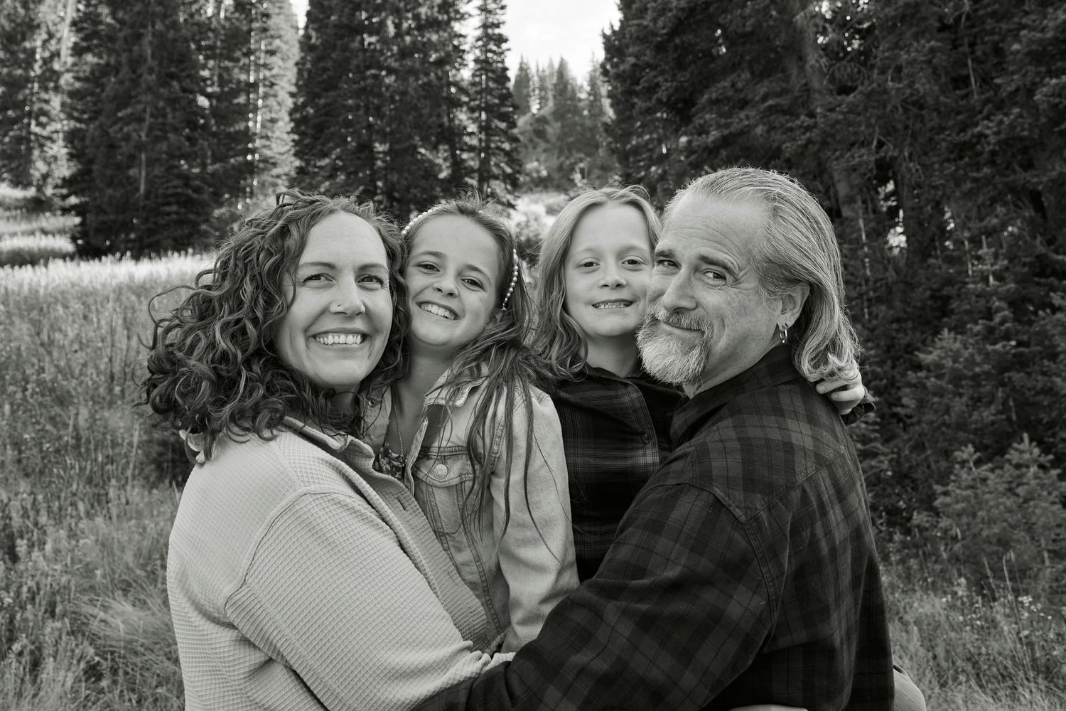Black and white family portrait in mountain meadow with evergreen forest background.
