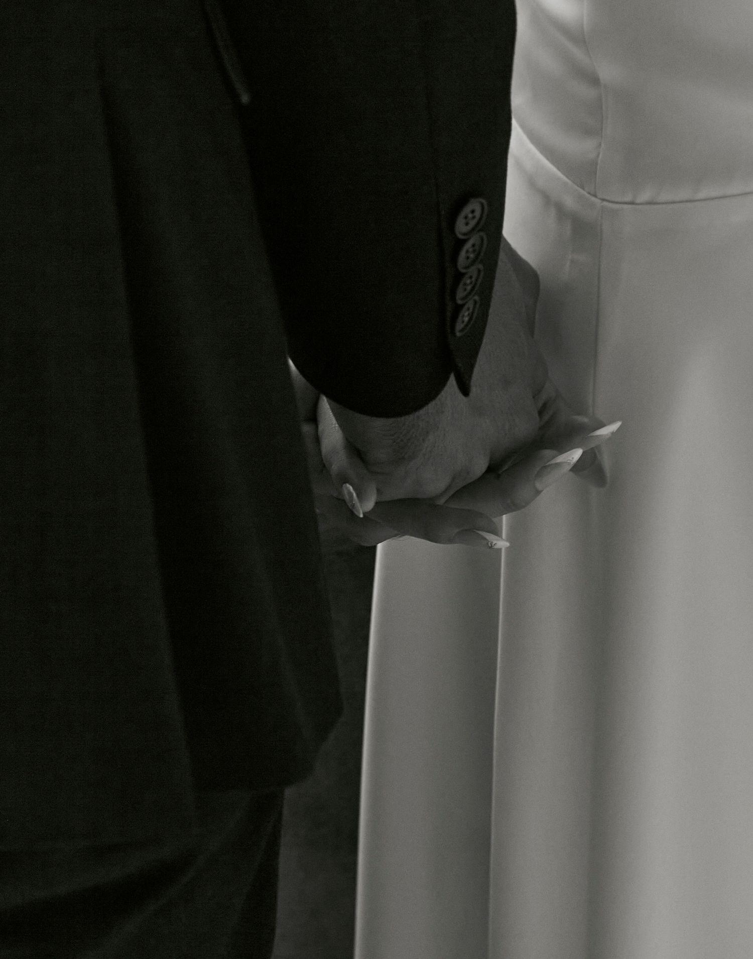Close-up black and white photo of clasped hands between formal attire.