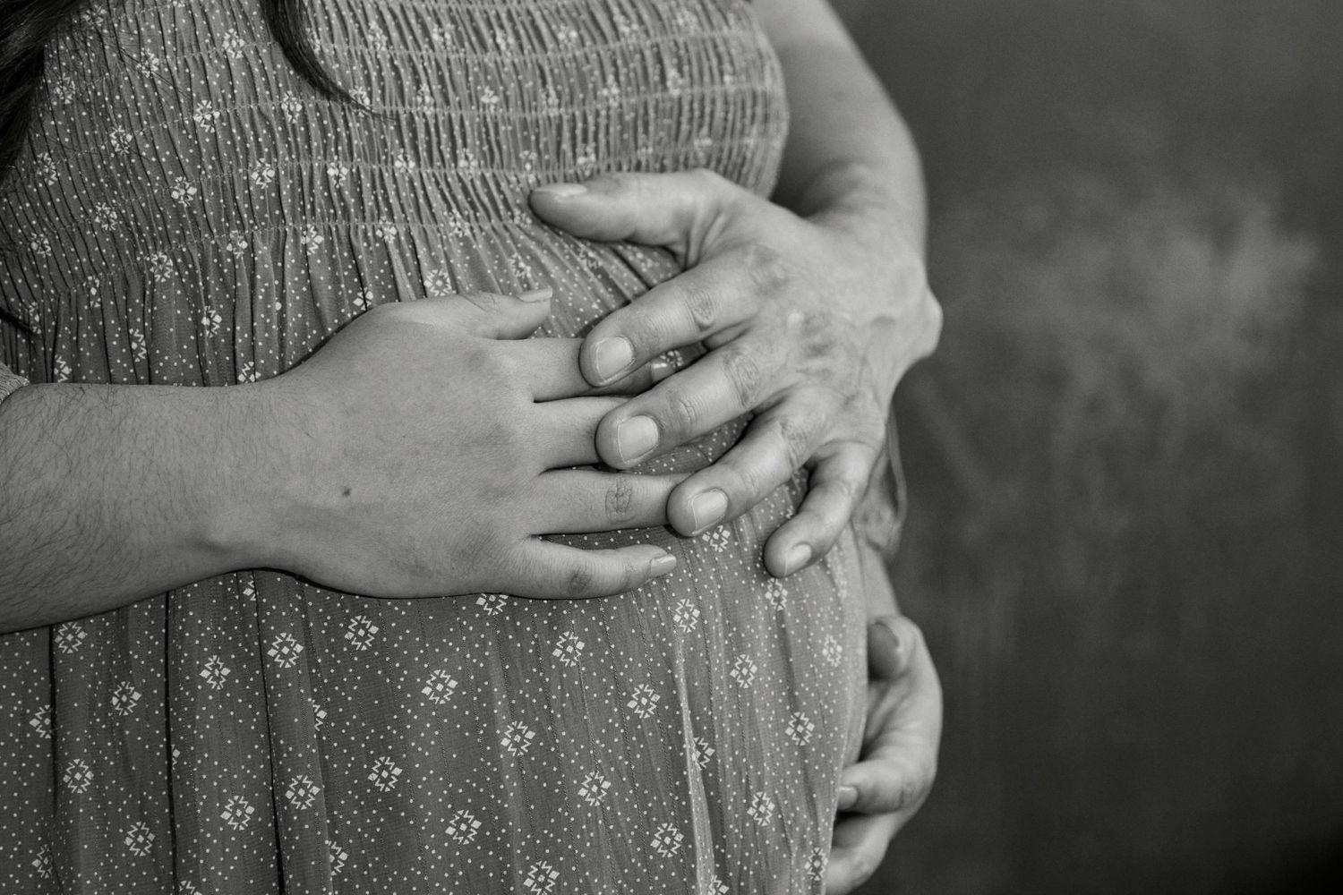 Black and white close-up of hands resting on a pregnant belly wearing a knit dress.