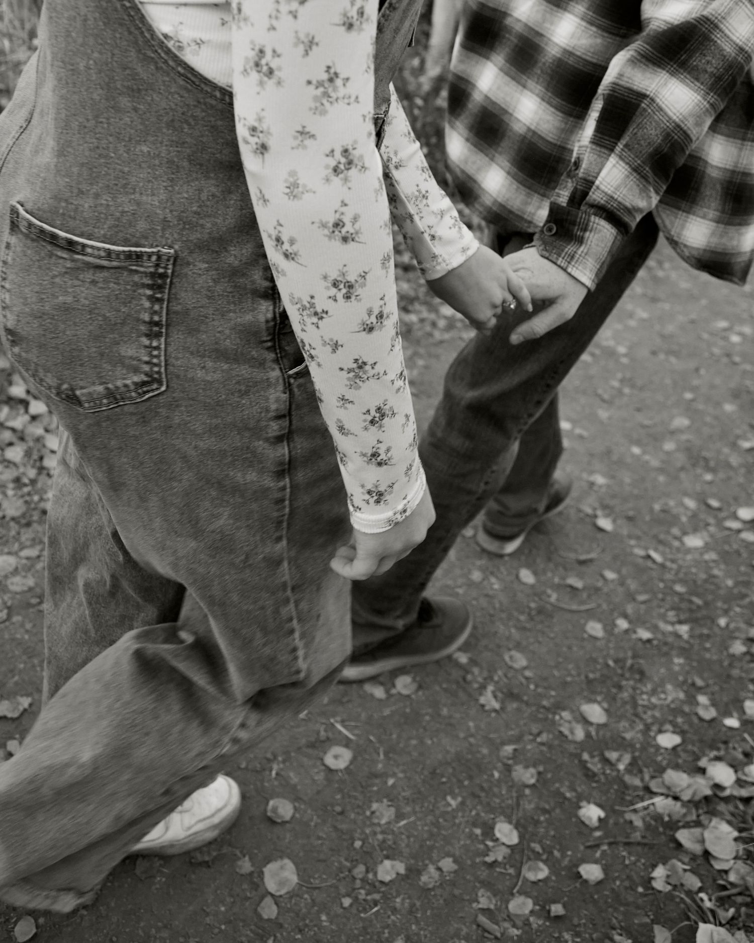 Close up of two people holding hands in jeans and casual clothing against a gravel surface.
