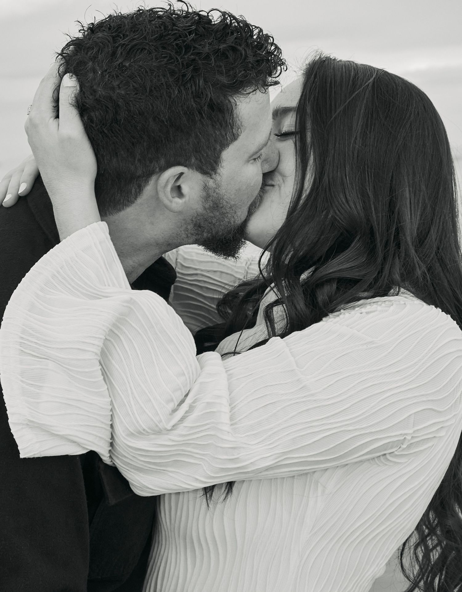 Romantic black and white portrait of a couple sharing an intimate kiss while wearing white sweaters.