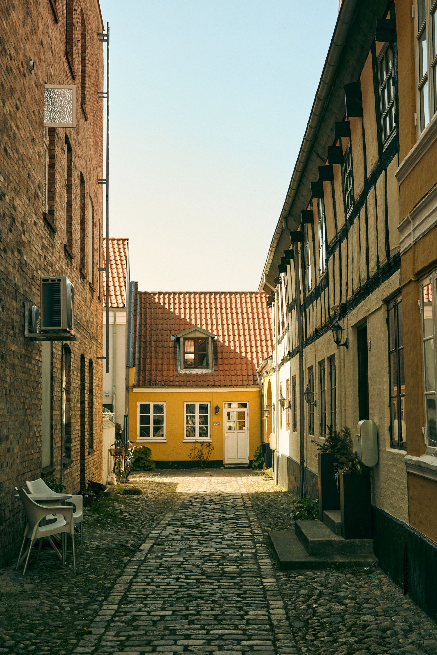 Narrow cobblestone alley with traditional European architecture and a yellow house at the end.