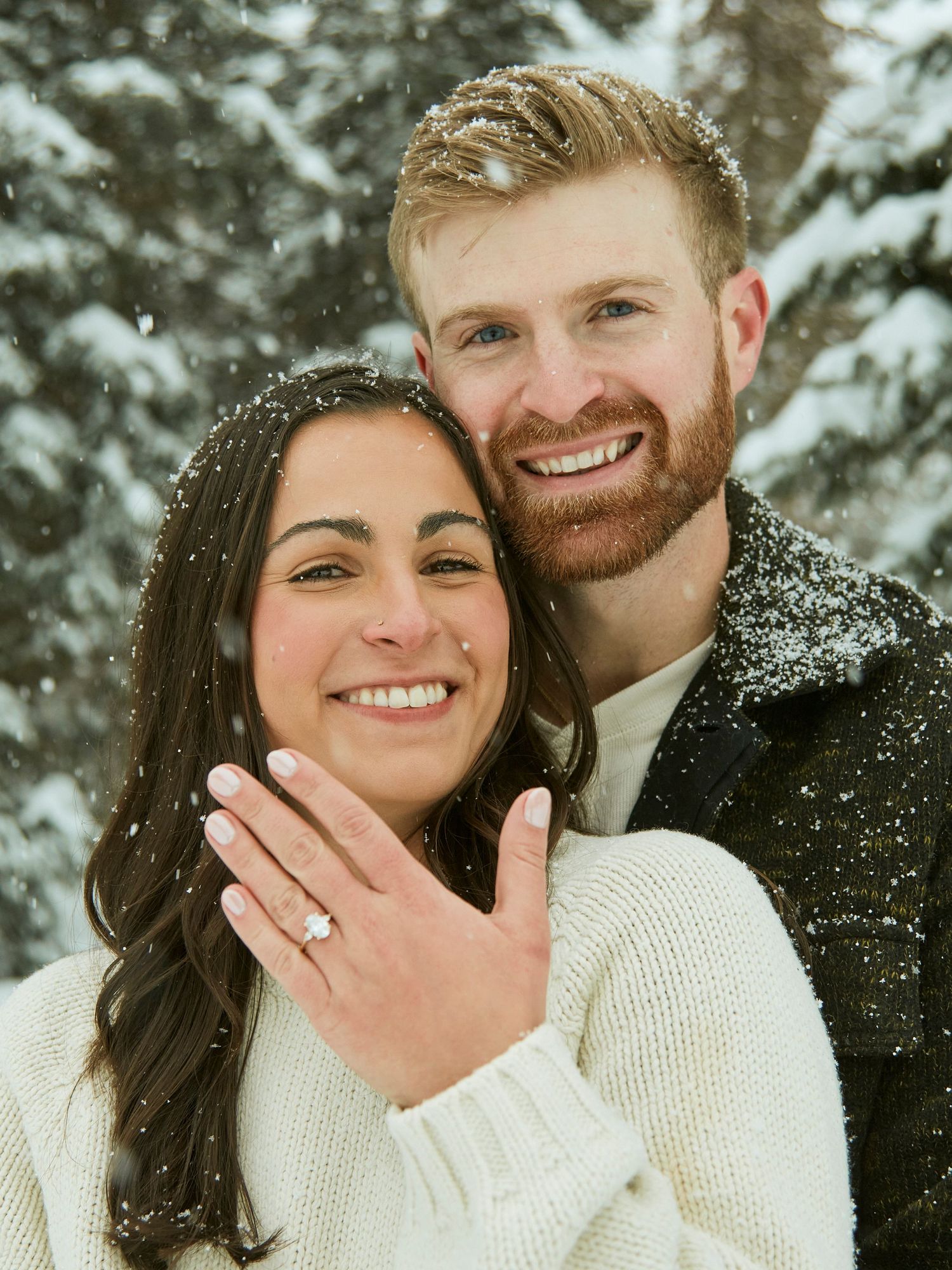 Engagement photo showing off ring in snowy winter forest setting.