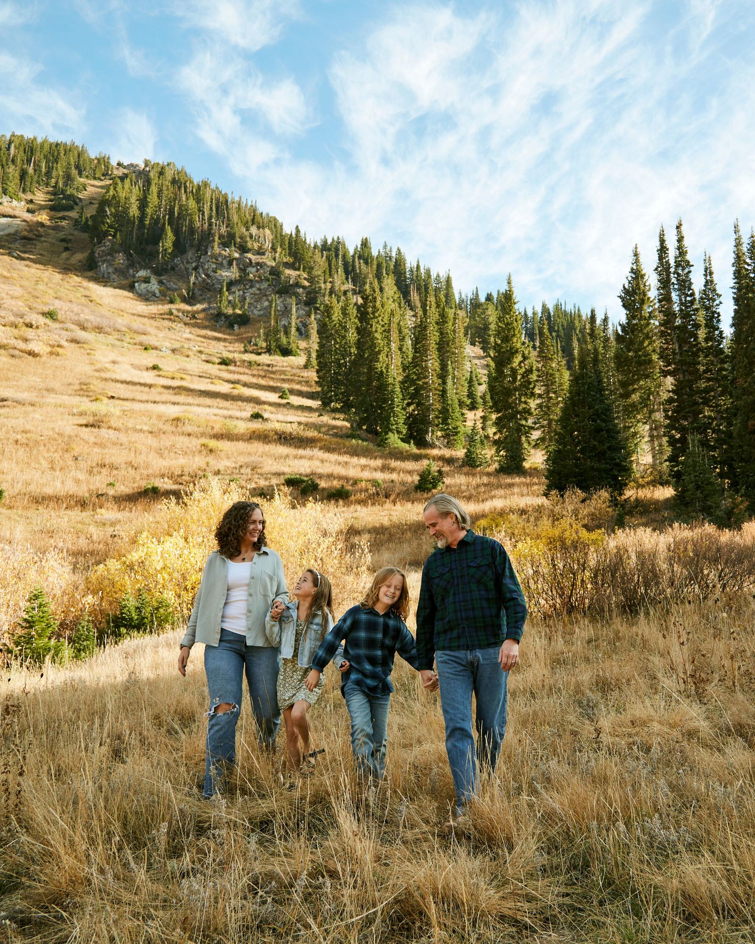 Family walking together on autumn mountainside with evergreen forest backdrop.