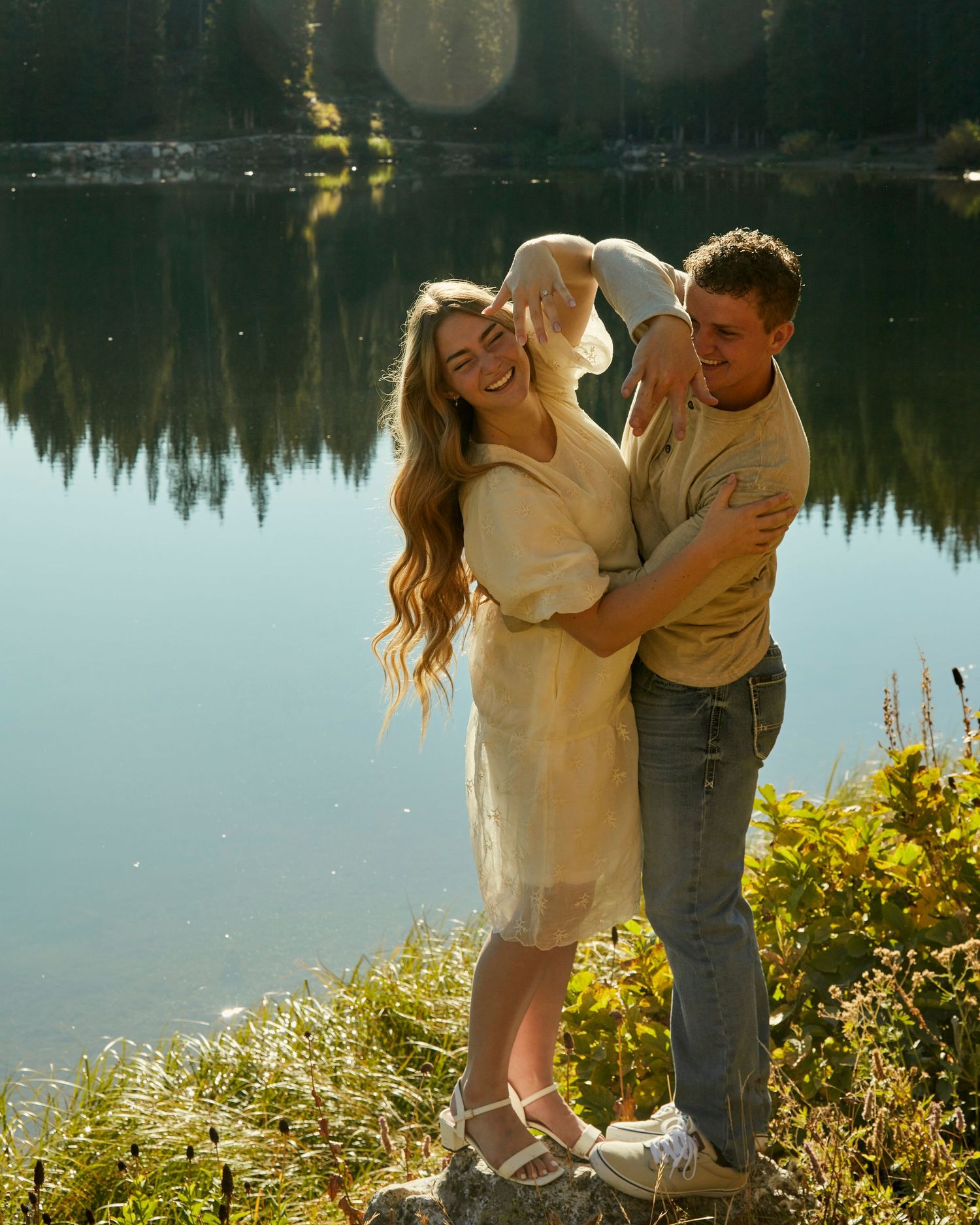 A romantic couple sharing a tender moment by a reflective lake during golden hour.