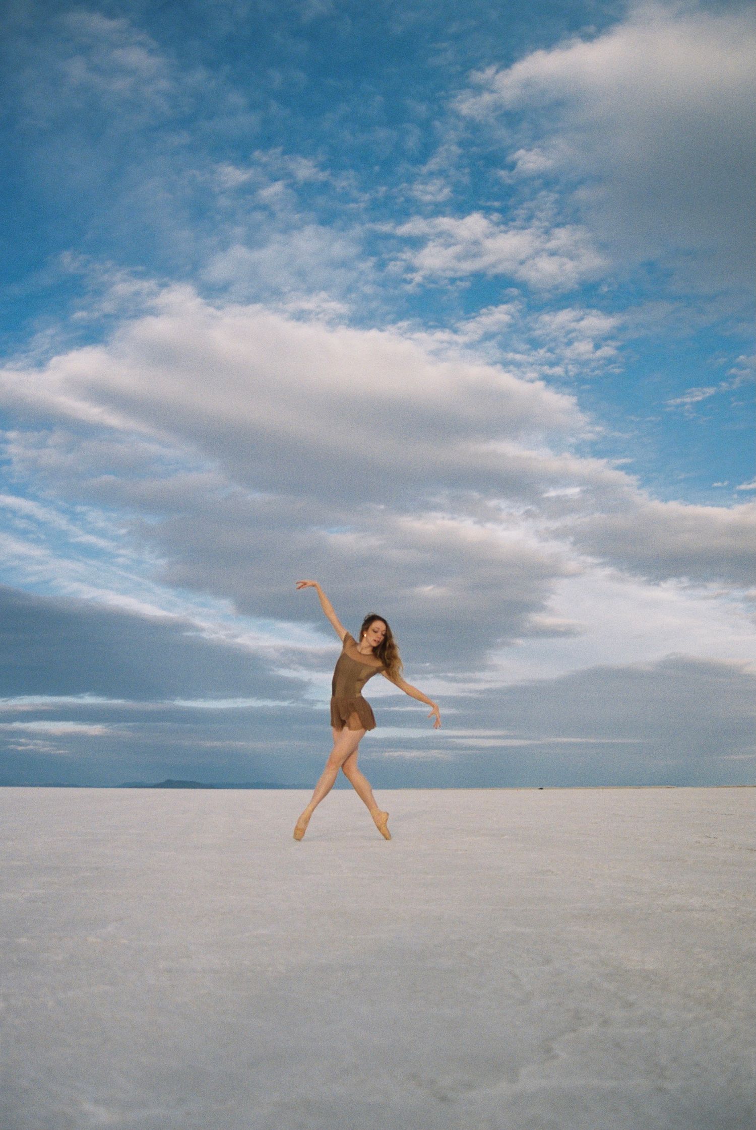 Dancer leaps gracefully across white salt flats beneath a cloudy blue sky.