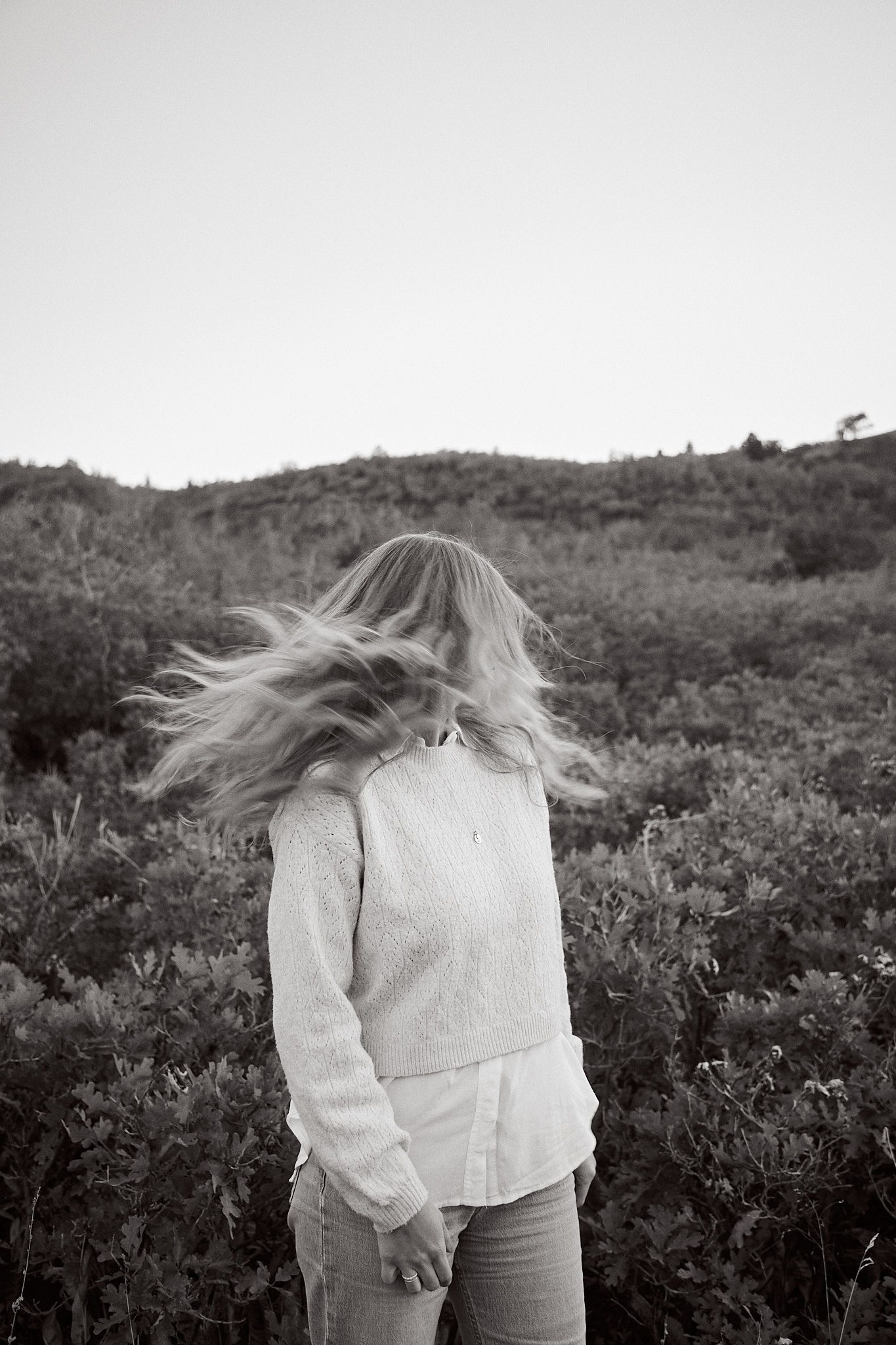 Black and white action shot capturing windswept hair against natural landscape.