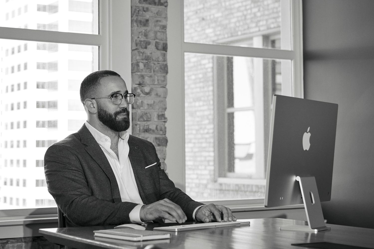 Professional working at desk with Apple iMac in modern office with exposed brick walls.