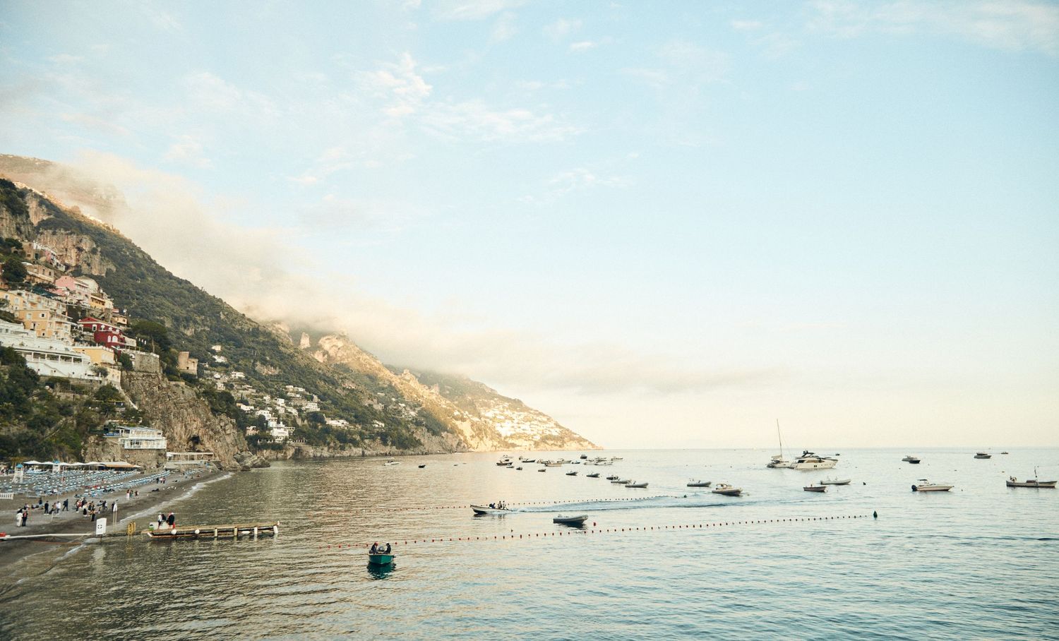 Vintage coastal view of boats dotting the Mediterranean waters along rocky cliffs at sunset.
