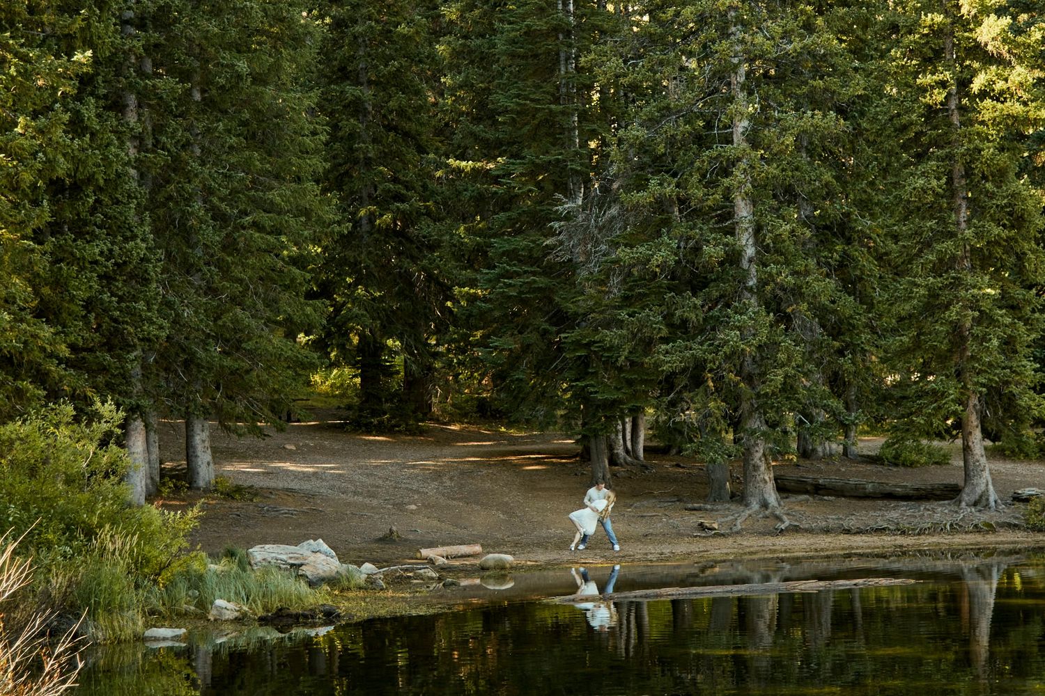 A tranquil lake scene with evergreen trees and people exploring the shoreline.