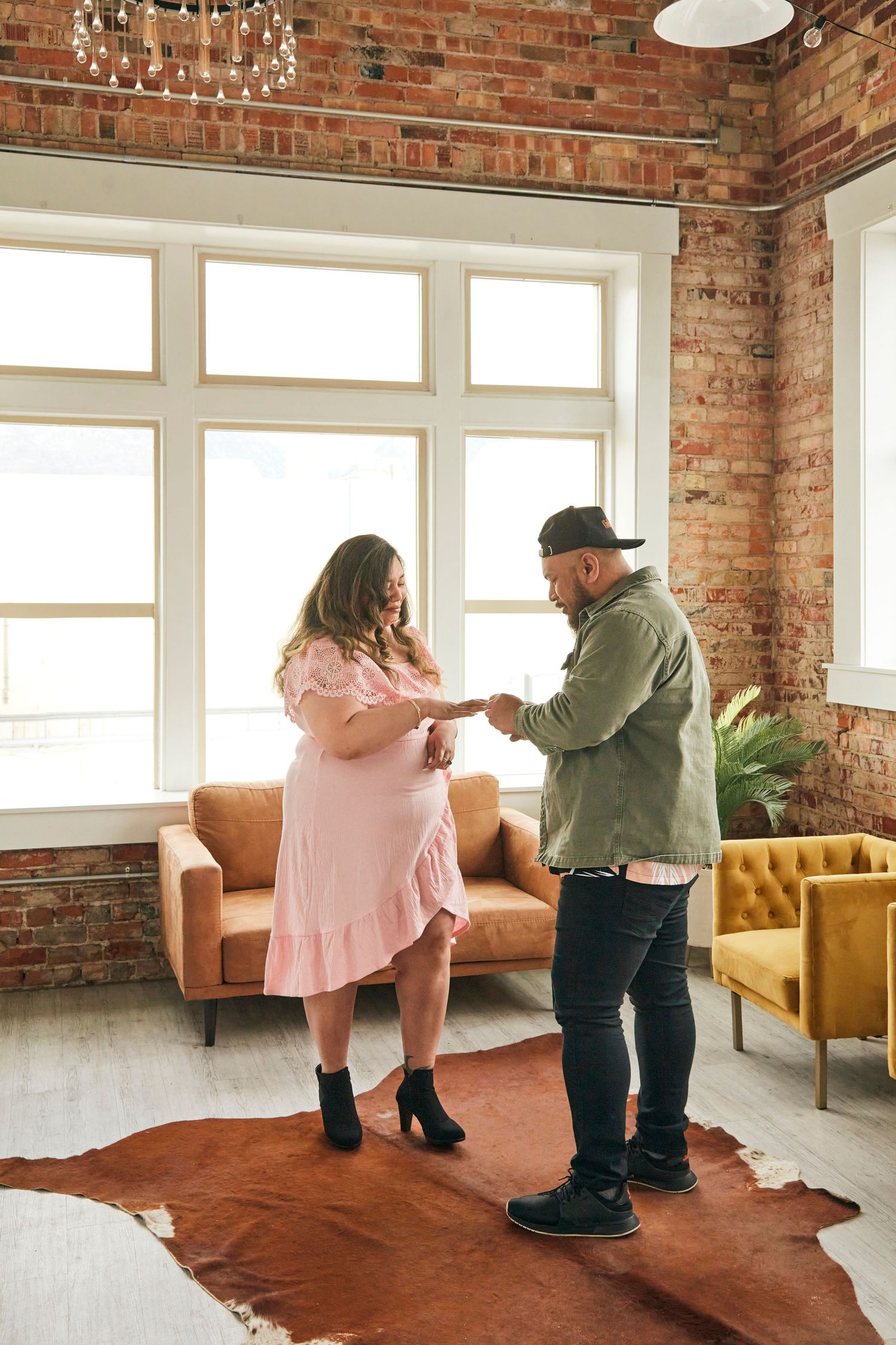 A couple dancing together on a brown cowhide rug in an industrial-style room with brick walls.
