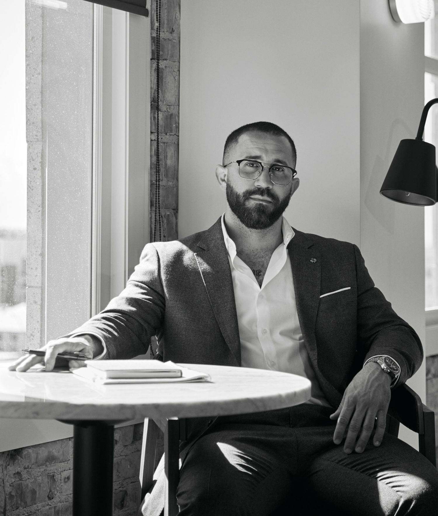 Business professional seated at table near window in modern office setting.