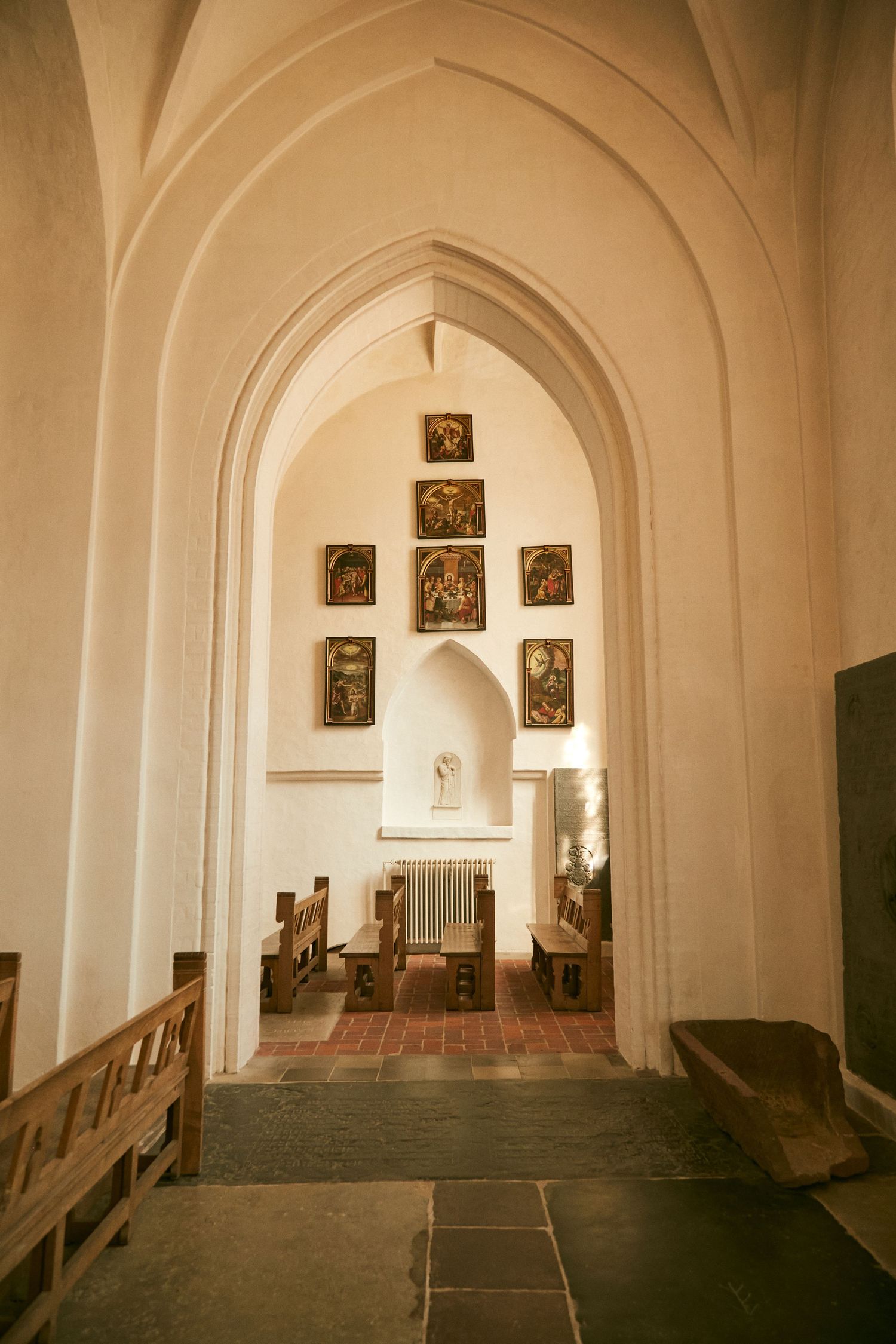 Gothic church interior with arched ceiling and religious artwork displayed on white walls.