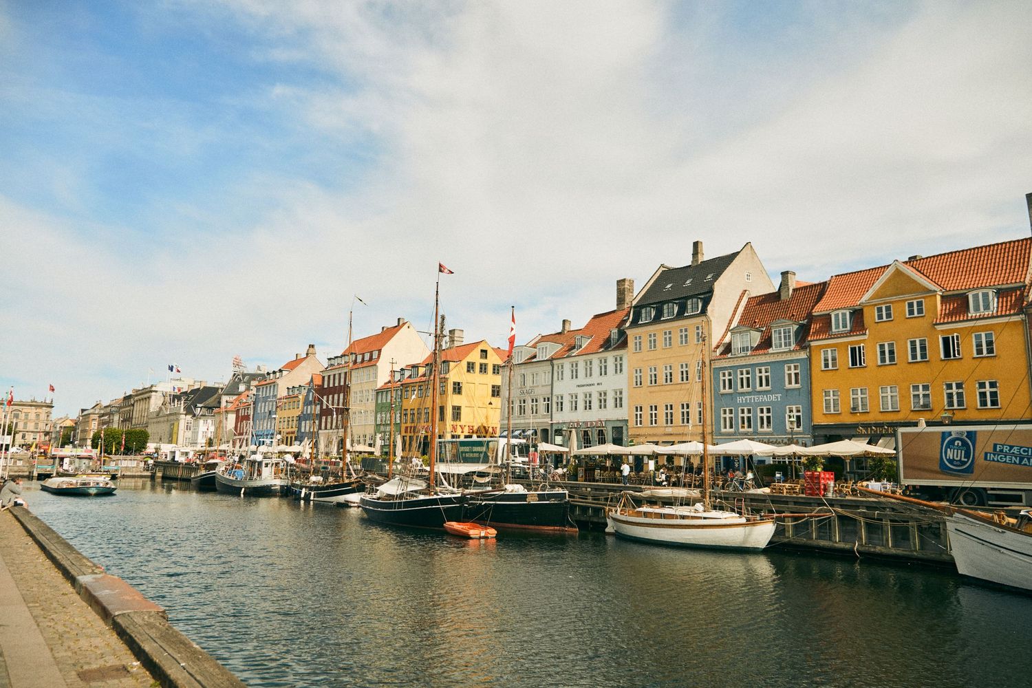 Colorful row of historic buildings and boats along Nyhavn canal in Copenhagen, Denmark.