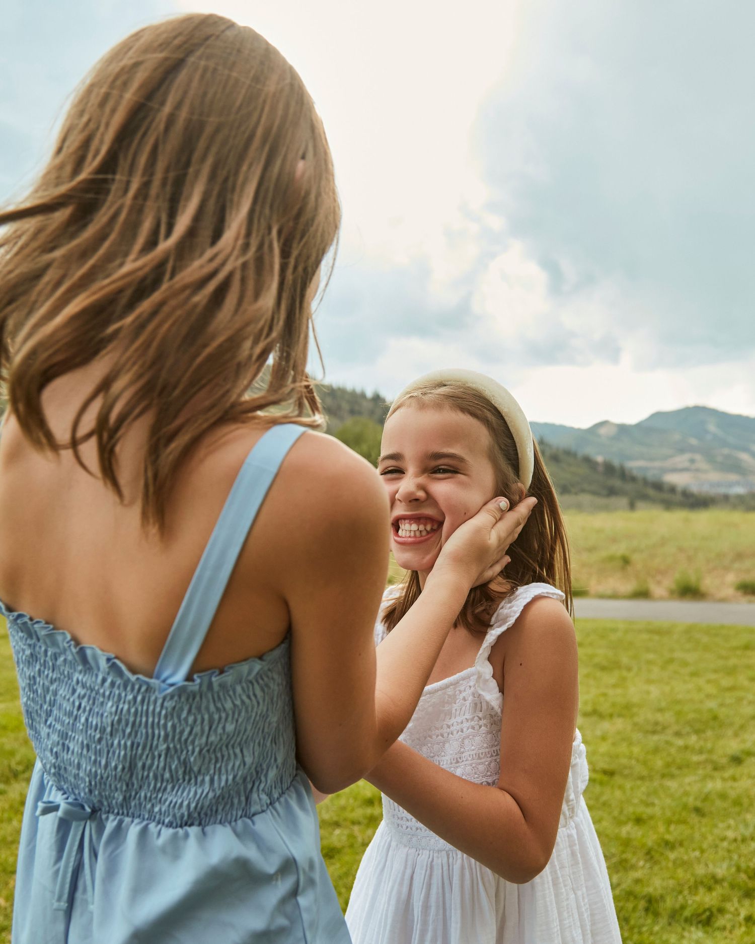 Two friends in summer dresses share a playful moment in a mountain meadow.