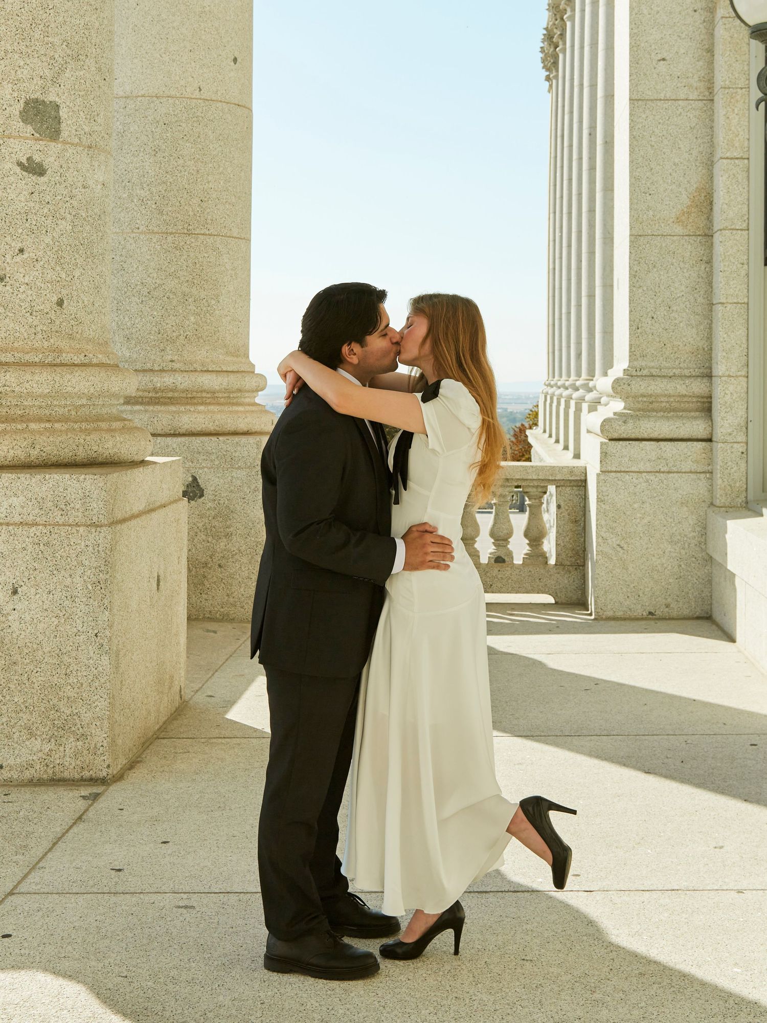 Romantic couple in formal attire sharing an intimate moment between classical columns.