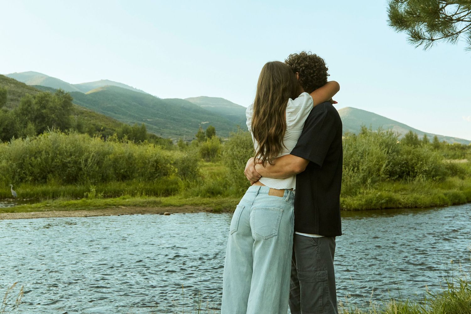 Romantic couple embracing by mountain stream during golden hour.
