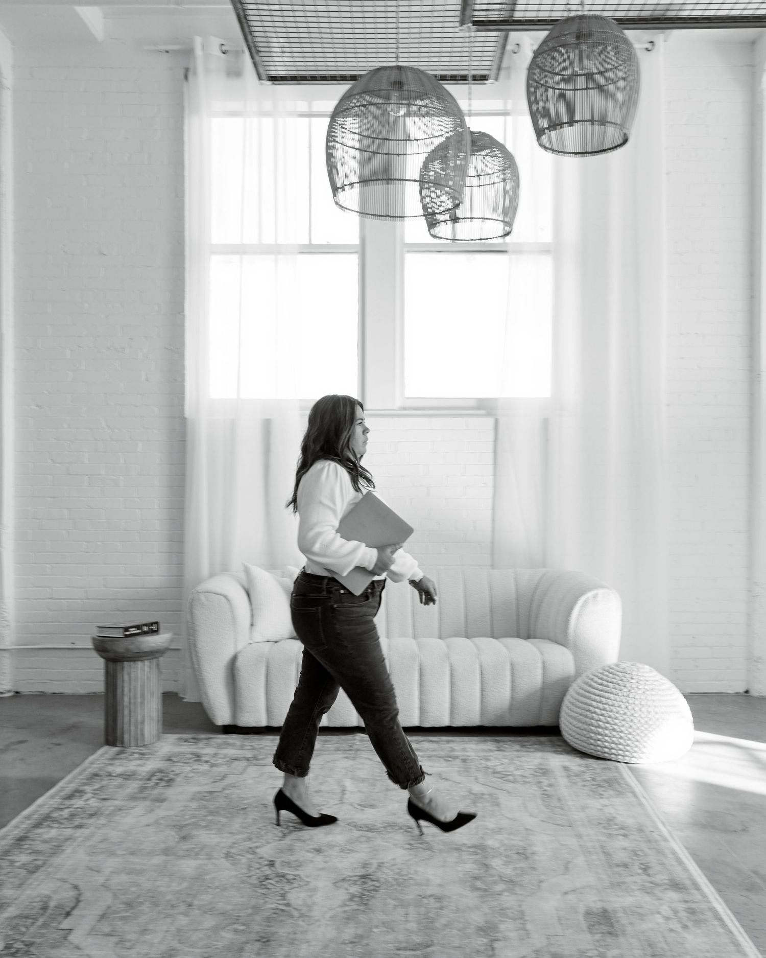 Professional woman walking confidently in modern white room with decorative pendant lights.