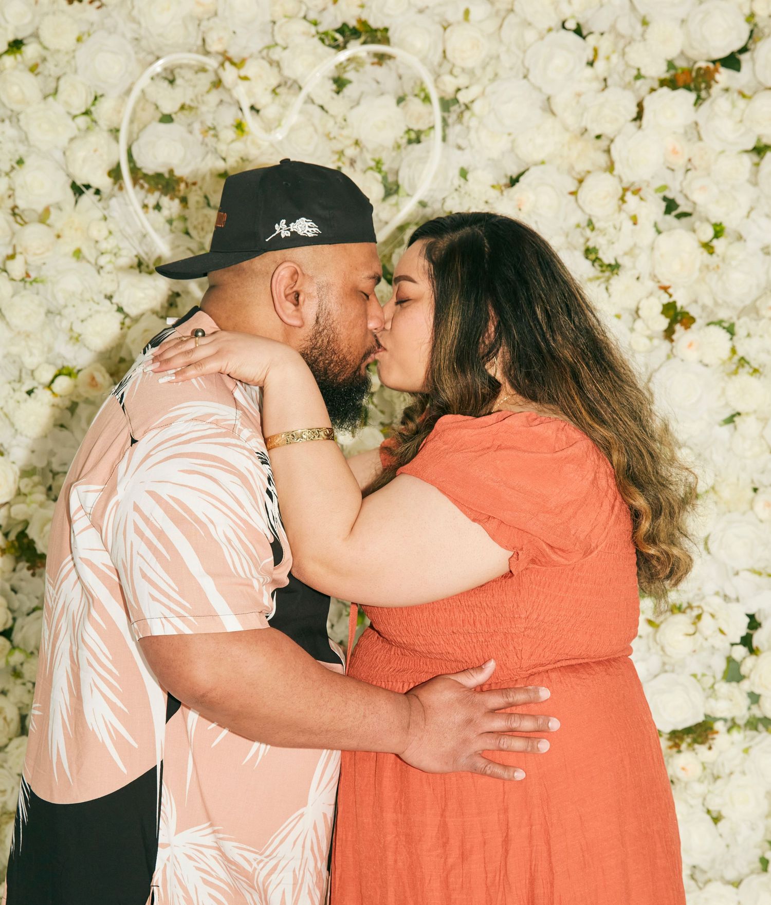A romantic moment captured against a white flower wall backdrop.