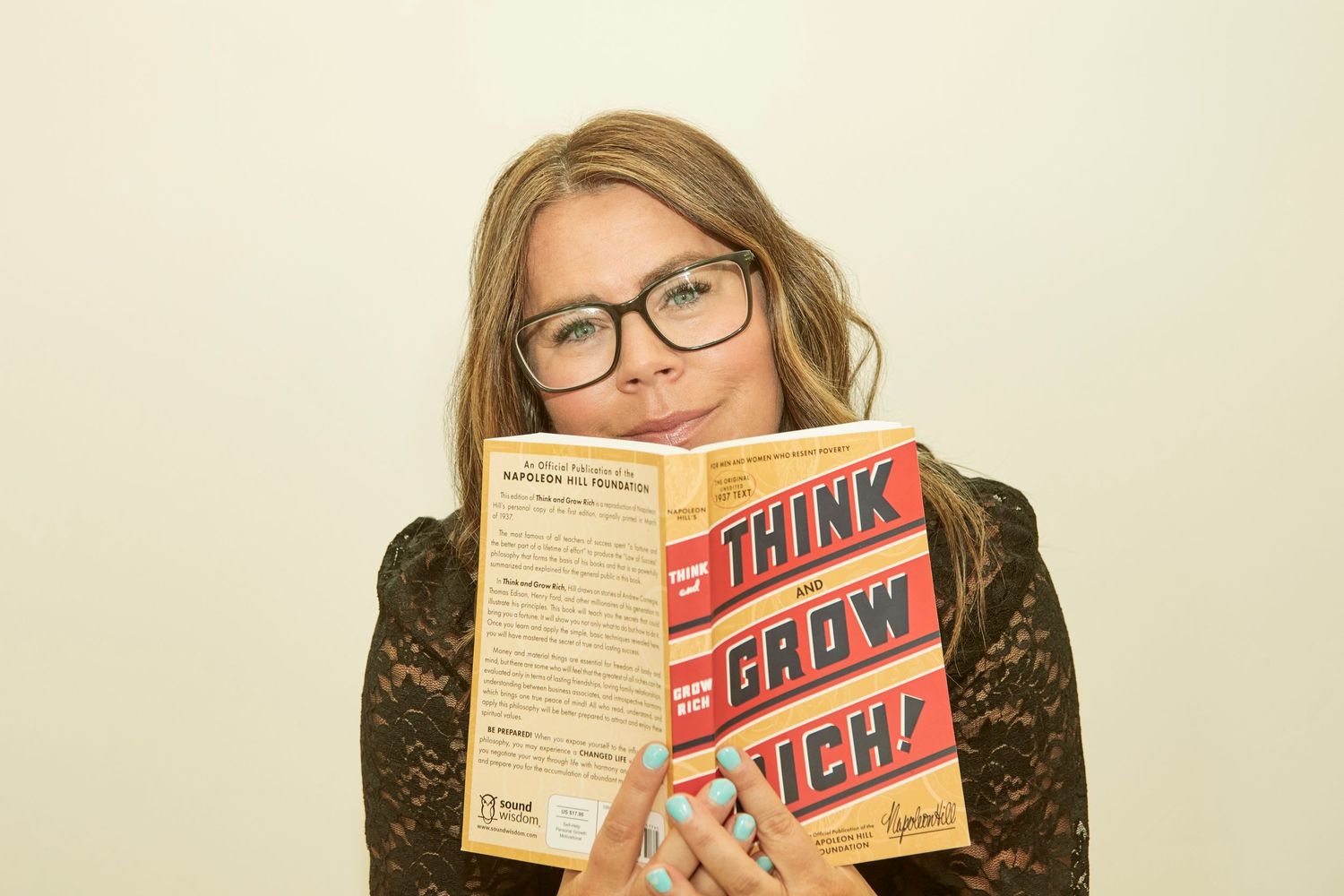 Lifestyle photo showing someone holding up the book 'Think Grow Rich' against neutral background.