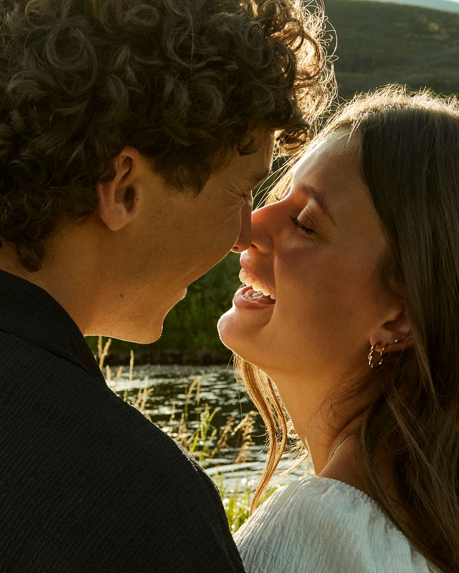 Couple sharing intimate moment in golden sunset light by water.