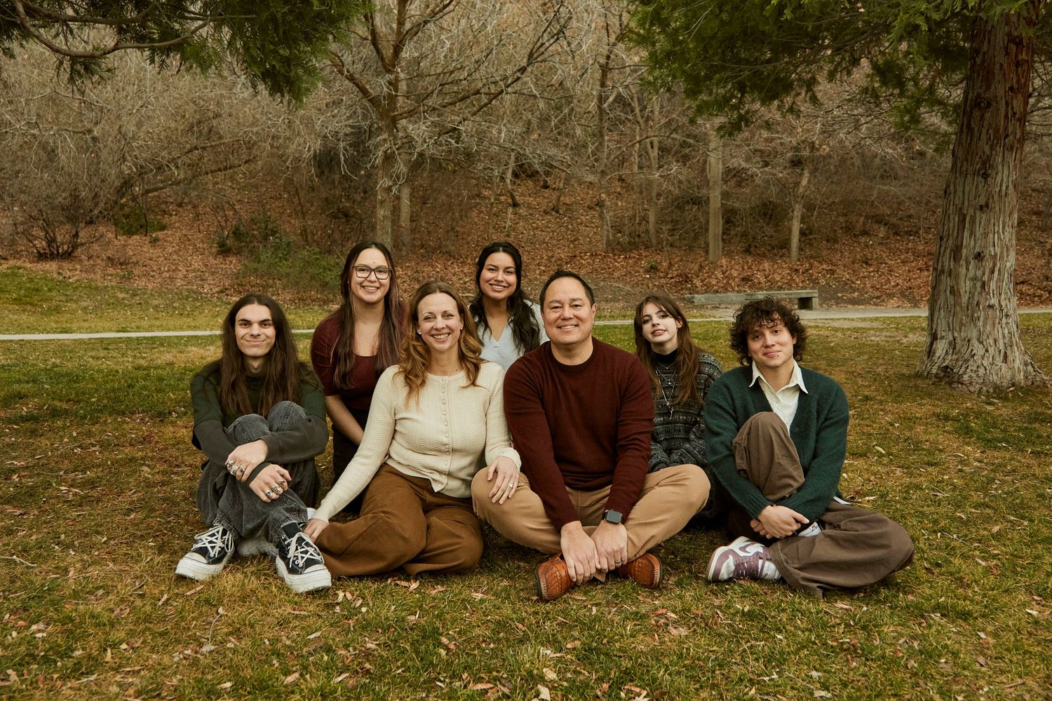 A group sits together on brown grass during autumn for a casual outdoor photo session.