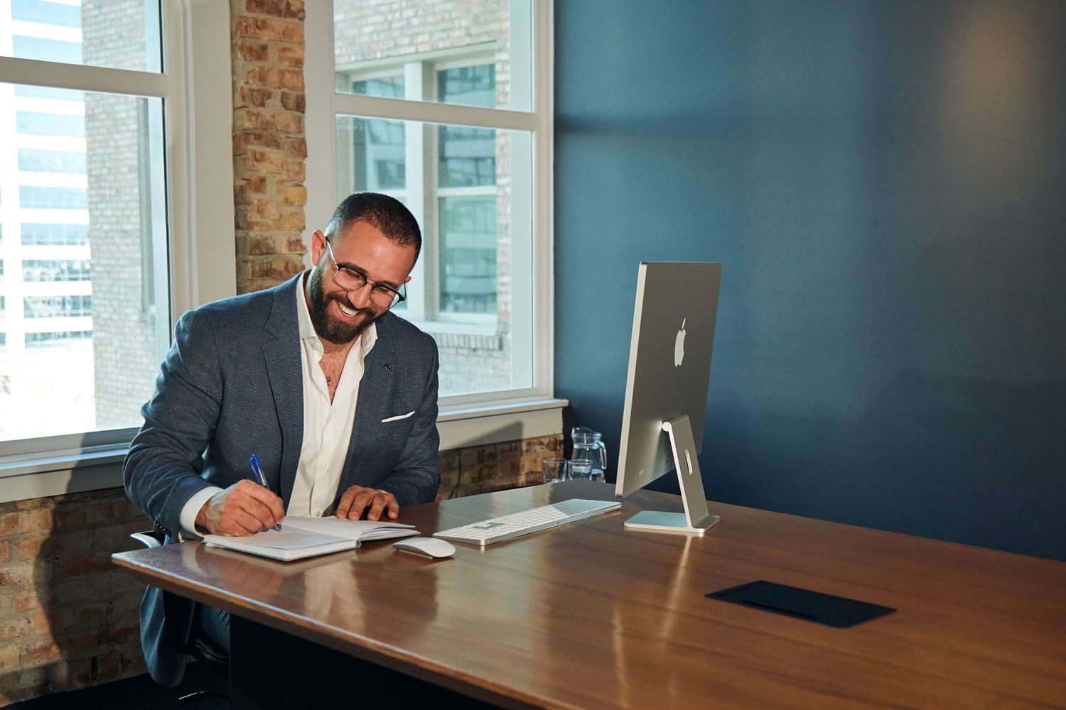 Professional businessman working at modern desk with iMac computer in bright office with exposed brick wall.