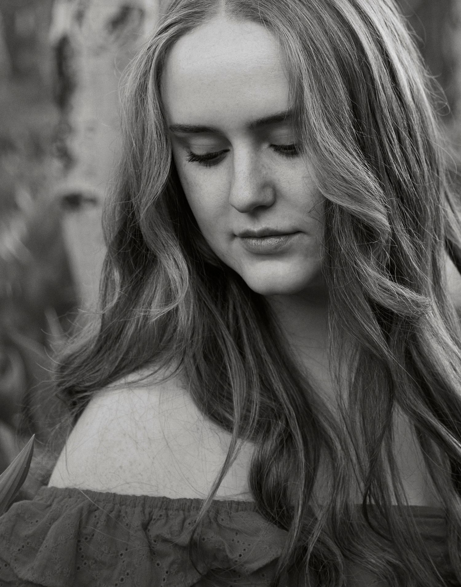 A black and white portrait showing soft waves of hair and an off-shoulder top.