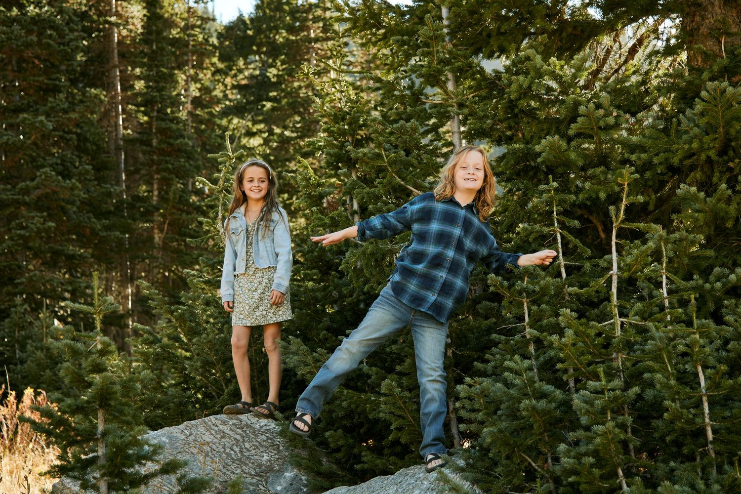 Two people posing playfully on rocky outcrop surrounded by evergreen forest.