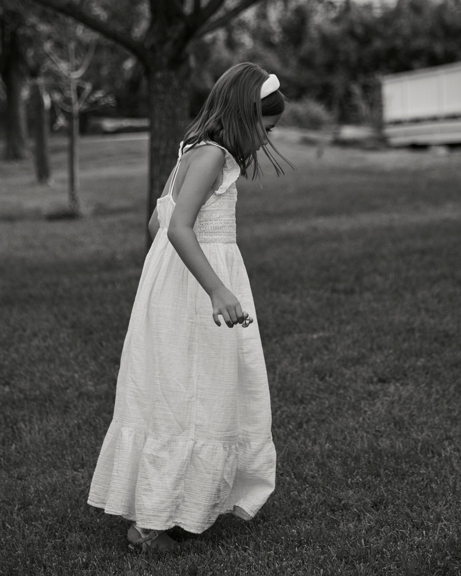 Black and white photo of person twirling in white dress on grassy lawn.
