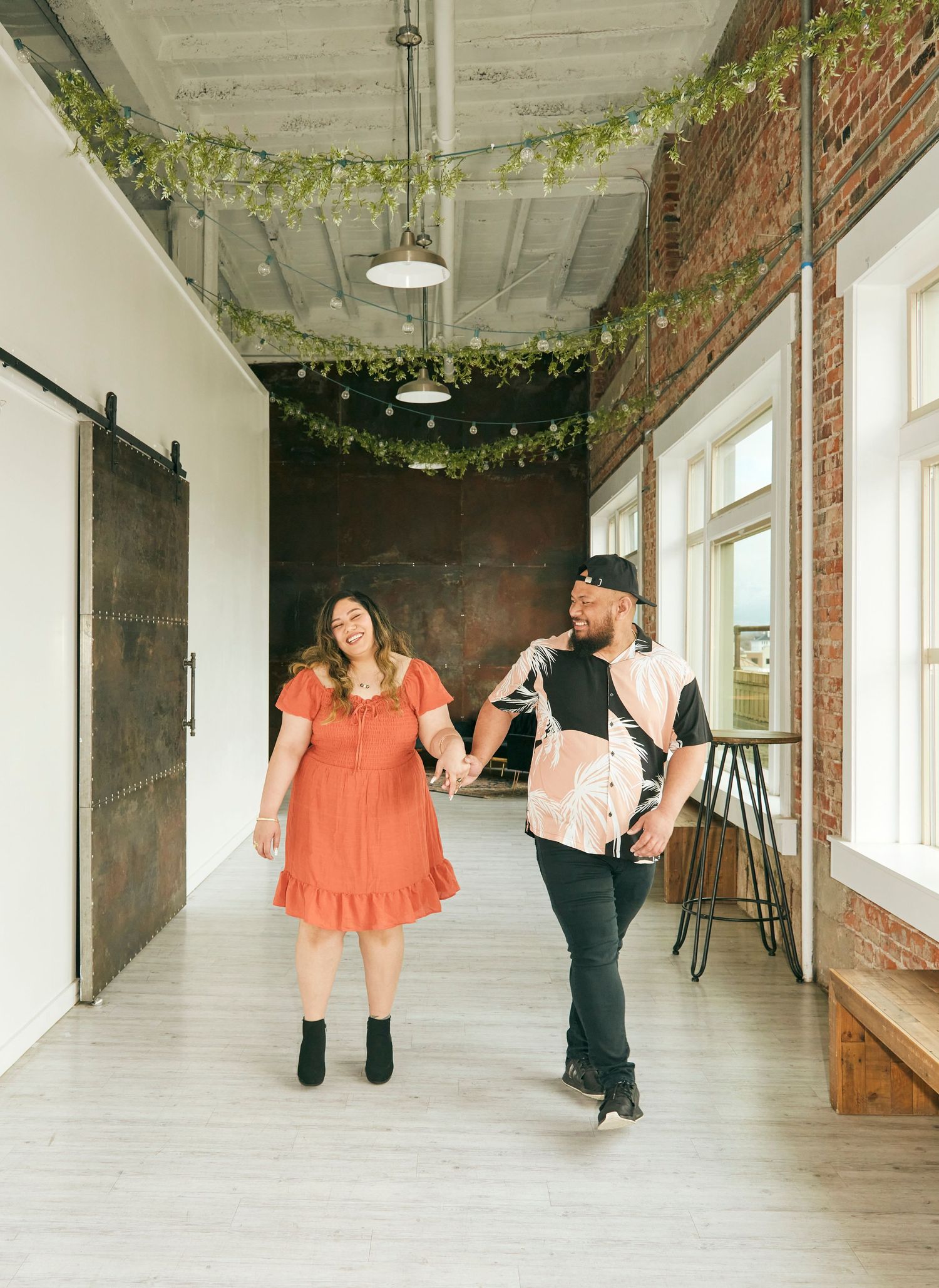 A couple walks together in an industrial-style hallway decorated with hanging greenery.