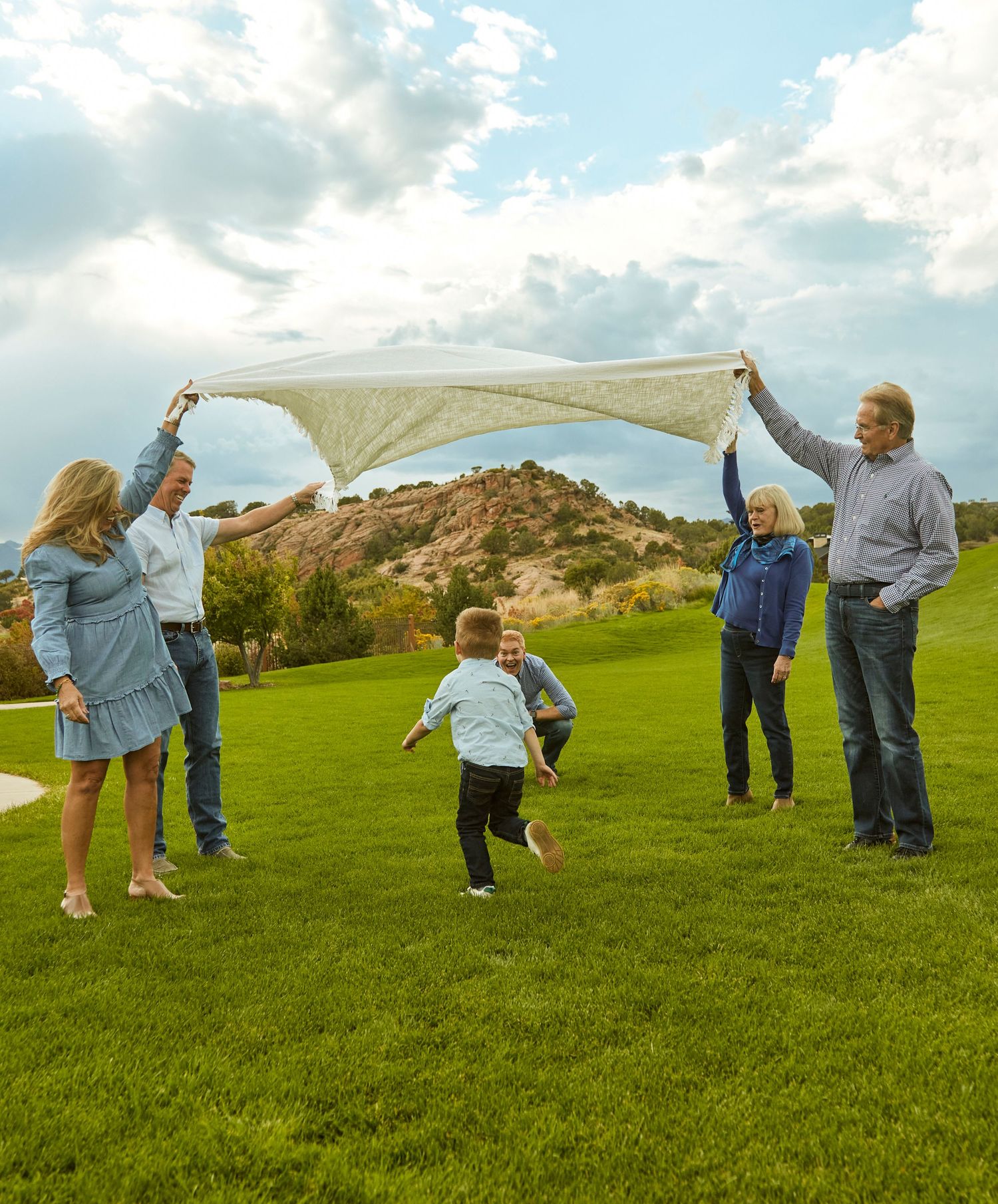 Group playing with a beige sheet in the air while running on grass.