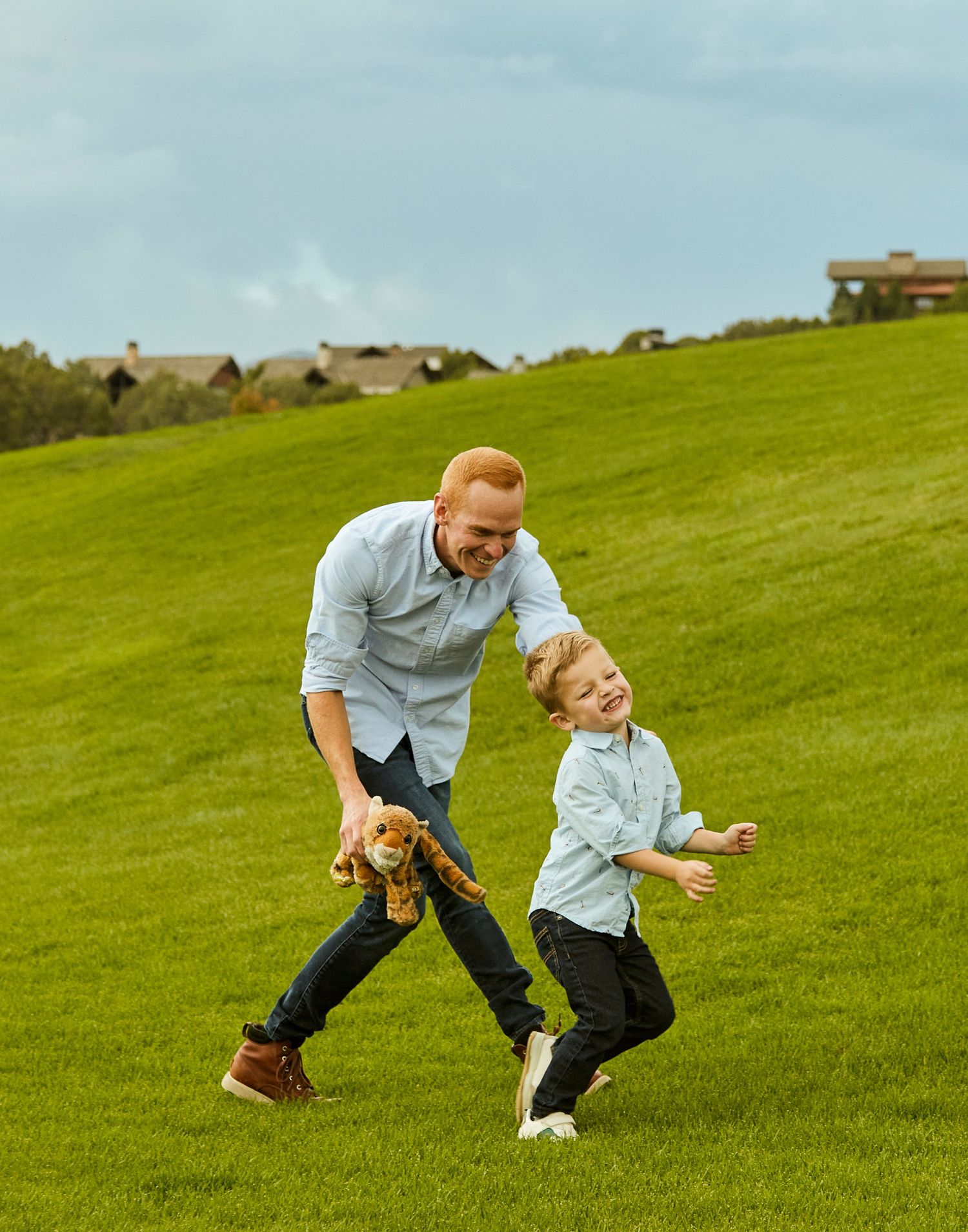 Running and playing together on a grassy hillside with a stuffed toy.