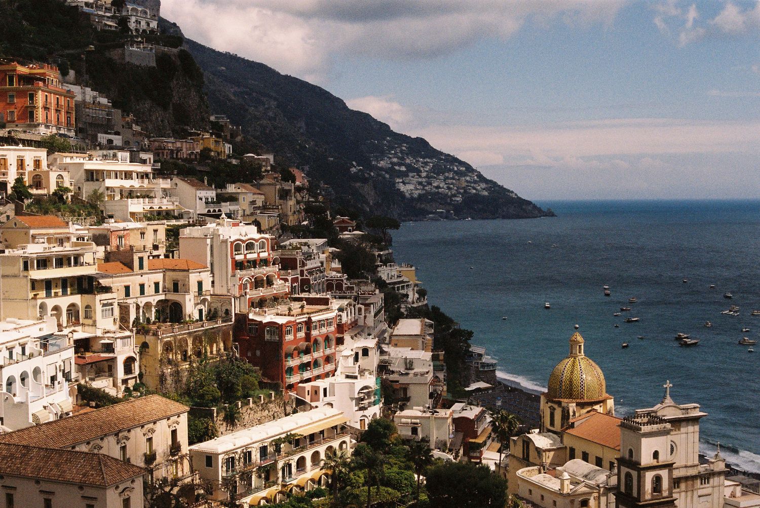 Colorful buildings cascade down the Amalfi Coast hillside with a golden-domed church overlooking the sea.