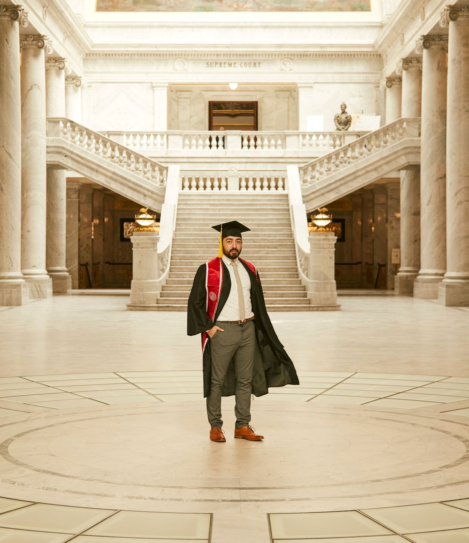 Graduation photo in grand marble hallway with classical columns and staircase.